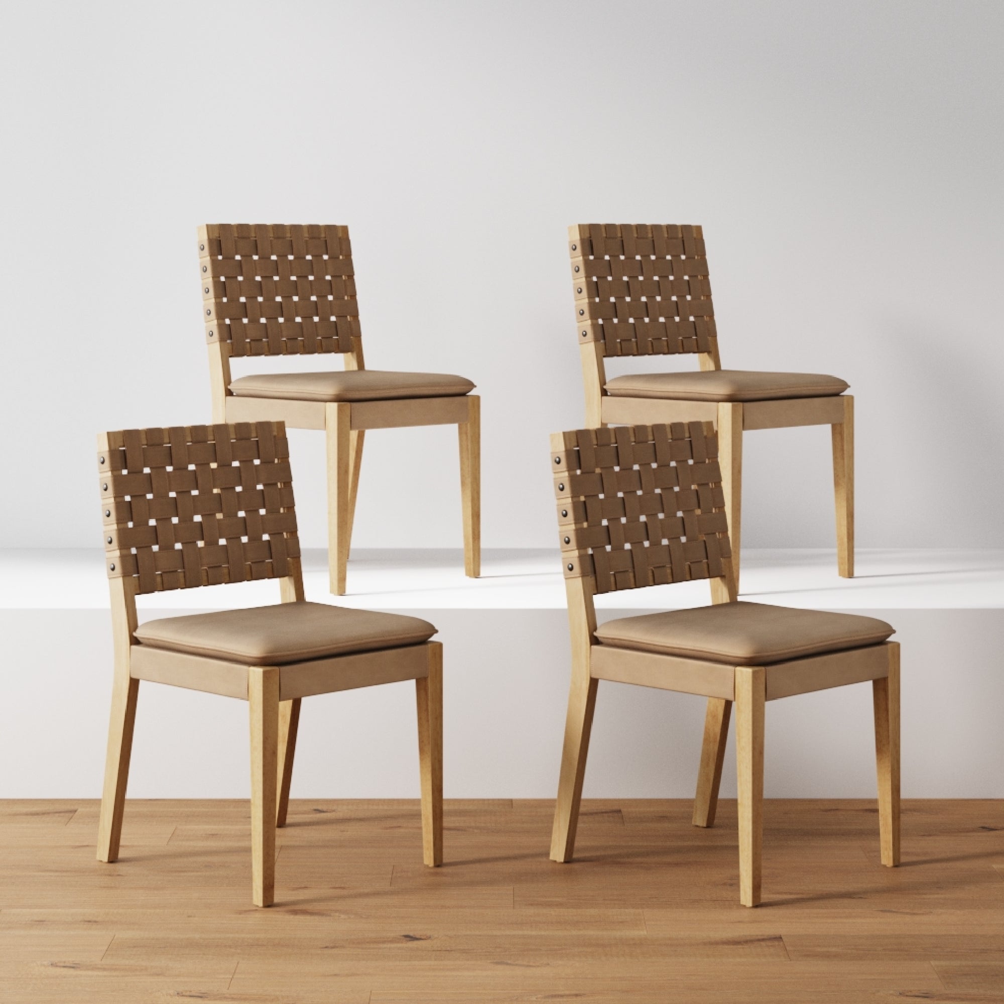 The Nathan James Faux Leather Dining Chairs Light Brown (Set of 4) feature hand-woven faux leather backrests, tan cushioned seats, and solid wood frames, shown on a wooden floor with two chairs on a white platform against a light wall.