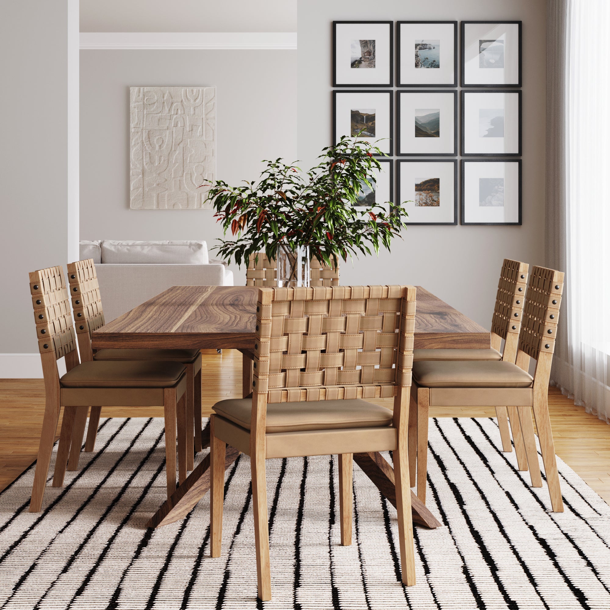 A modern dining room with a solid wood table, six Nathan James Faux Leather Dining Chairs in light brown, a plant centerpiece, striped rug, and wall art in a bright space with wooden floors.