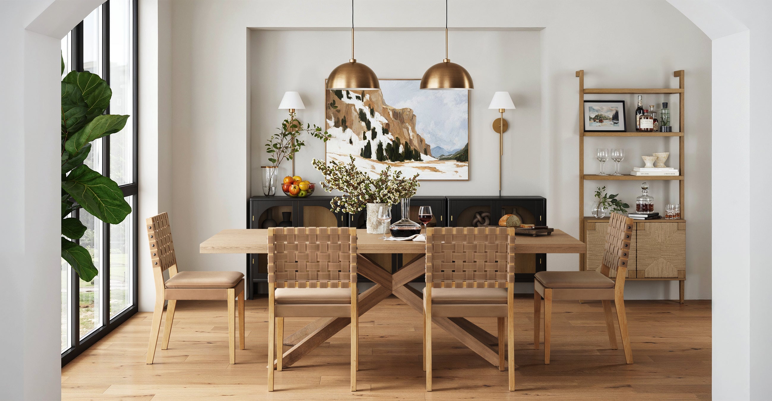Modern dining room with a light wooden table and woven chairs, pendant lights above, a landscape painting on the back wall, plants, and shelves with glassware and decor. Large window lets in natural light.