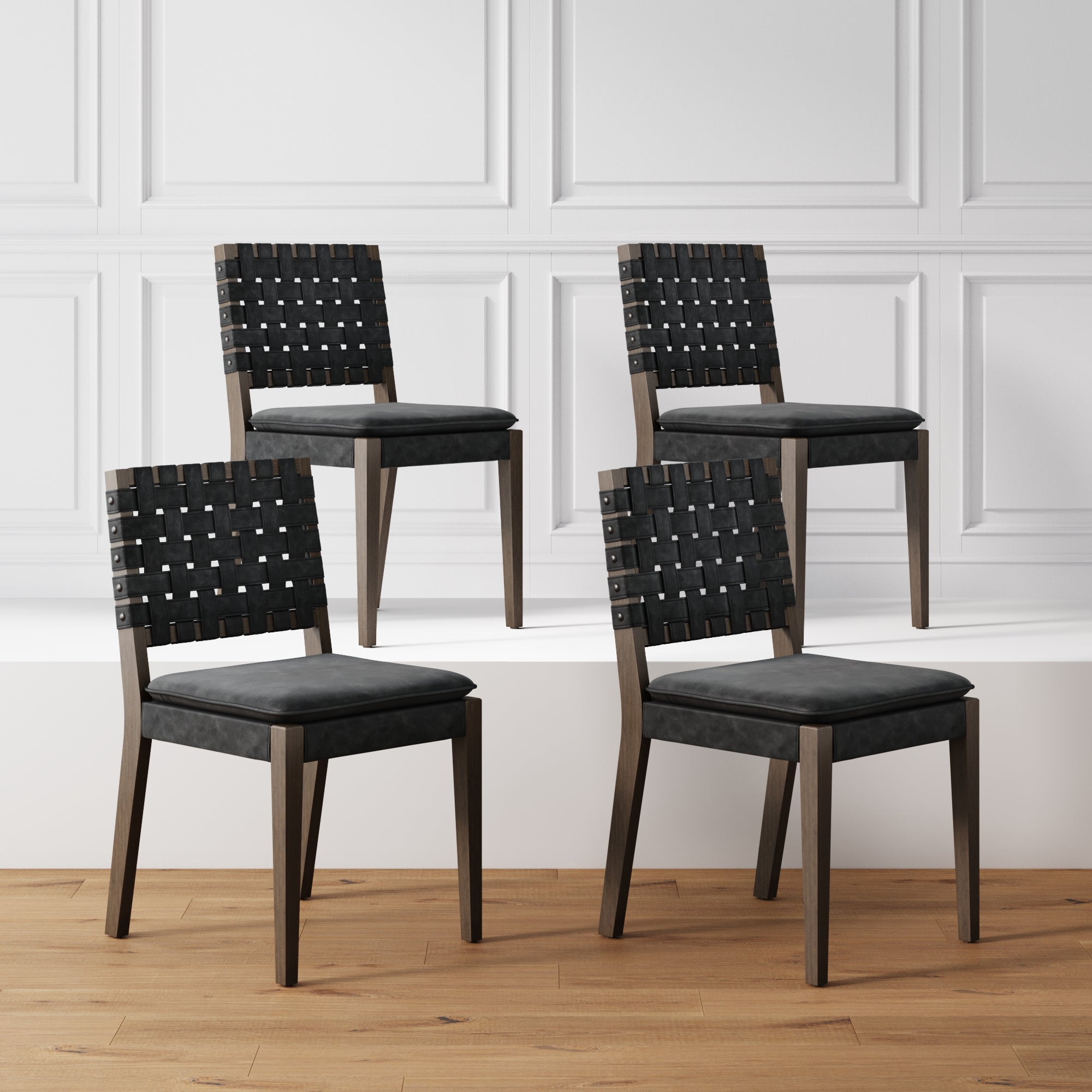 Four Nathan James Faux Leather Dining Chairs in black, sold as a set of 4, are displayed on a wooden floor and white platform against a white paneled wall.