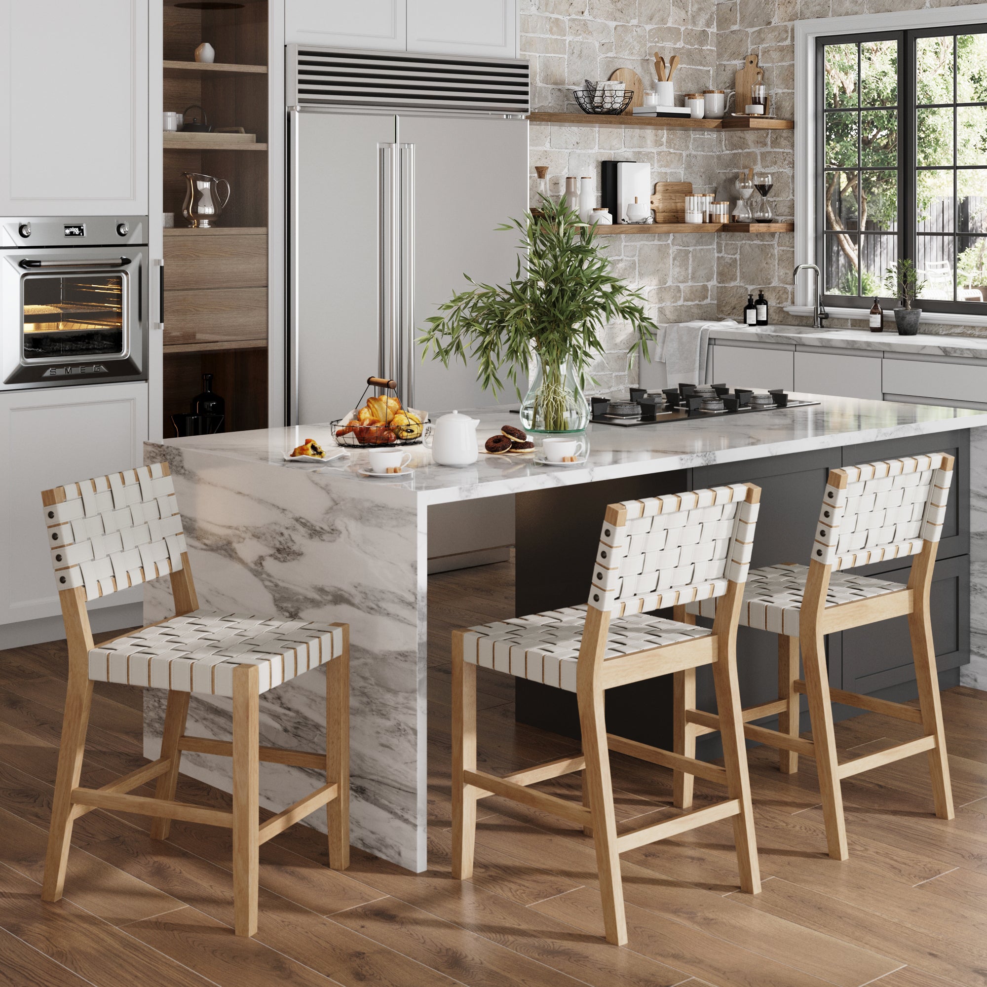 A modern kitchen features a marble island, a set of three Nathan James Off White Faux Leather Woven Counter Height Bar Stools, breakfast items, plants, a large window, white cabinets, and stainless steel appliances.