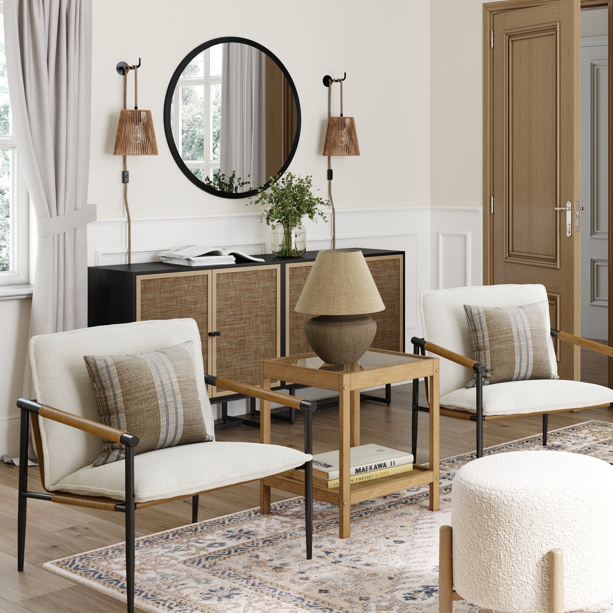 A modern living room features two Nathan James Boucle & Metal Accent Chairs, a wooden side table with a lamp, a patterned rug, and a black console topped with a round mirror. Neutral tones and natural light create an inviting space.