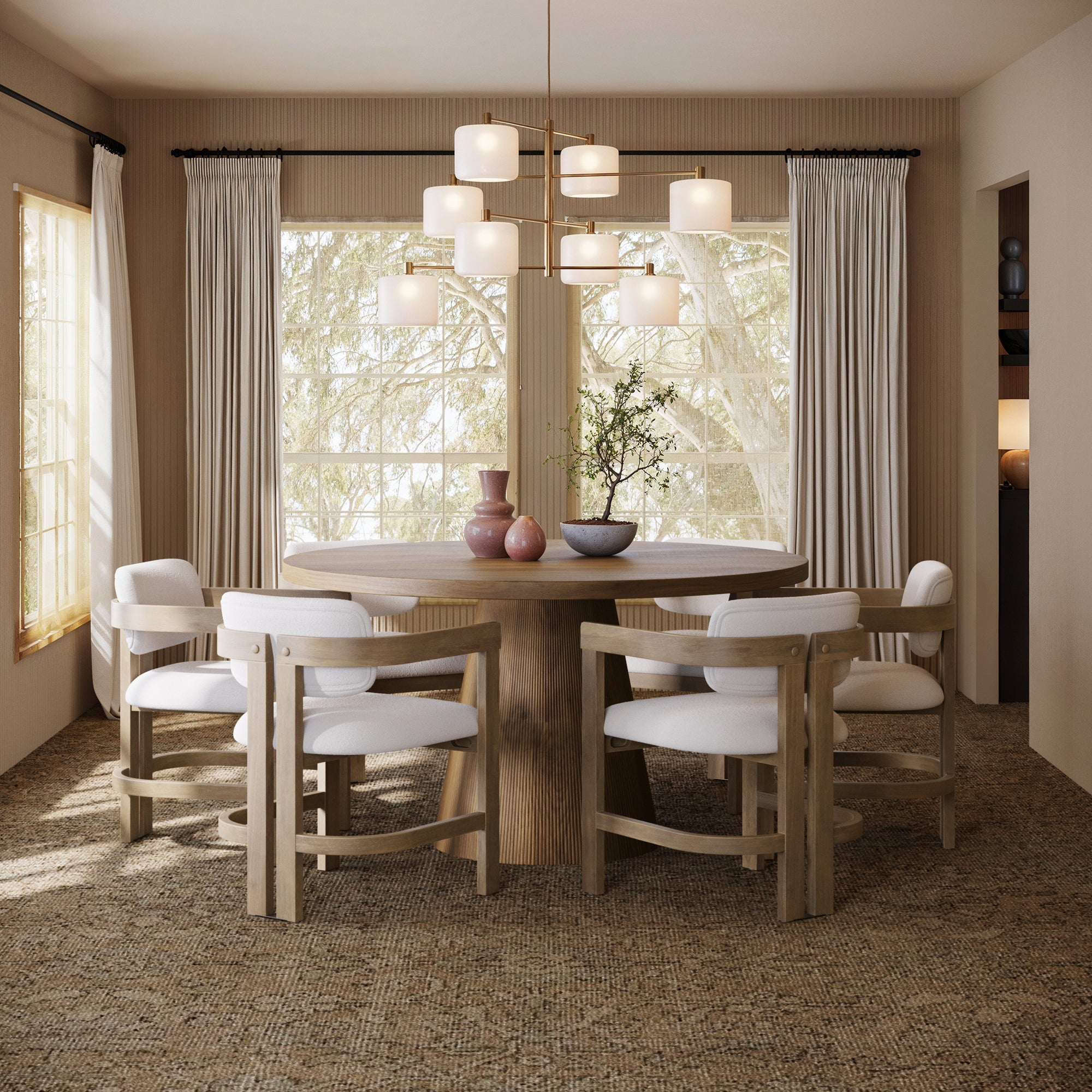 A modern dining room features the Nathan James Boucle Dining Chair w/ Curved Back and Arm in light brown (set of 6), surrounding a round wooden table, with neutral decor, white curtains, a beige carpet, vases, and a contemporary chandelier.