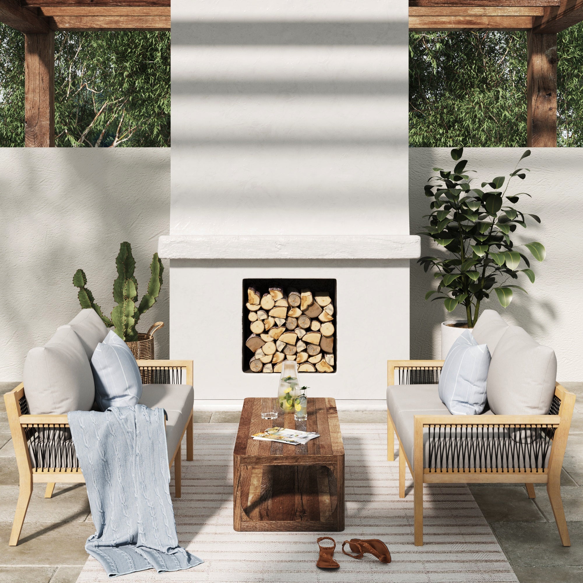 A modern outdoor patio with two cushioned wooden chairs, a wooden coffee table, a fireplace stacked with logs, potted plants, a striped rug, and a light blue throw blanket draped over a chair.