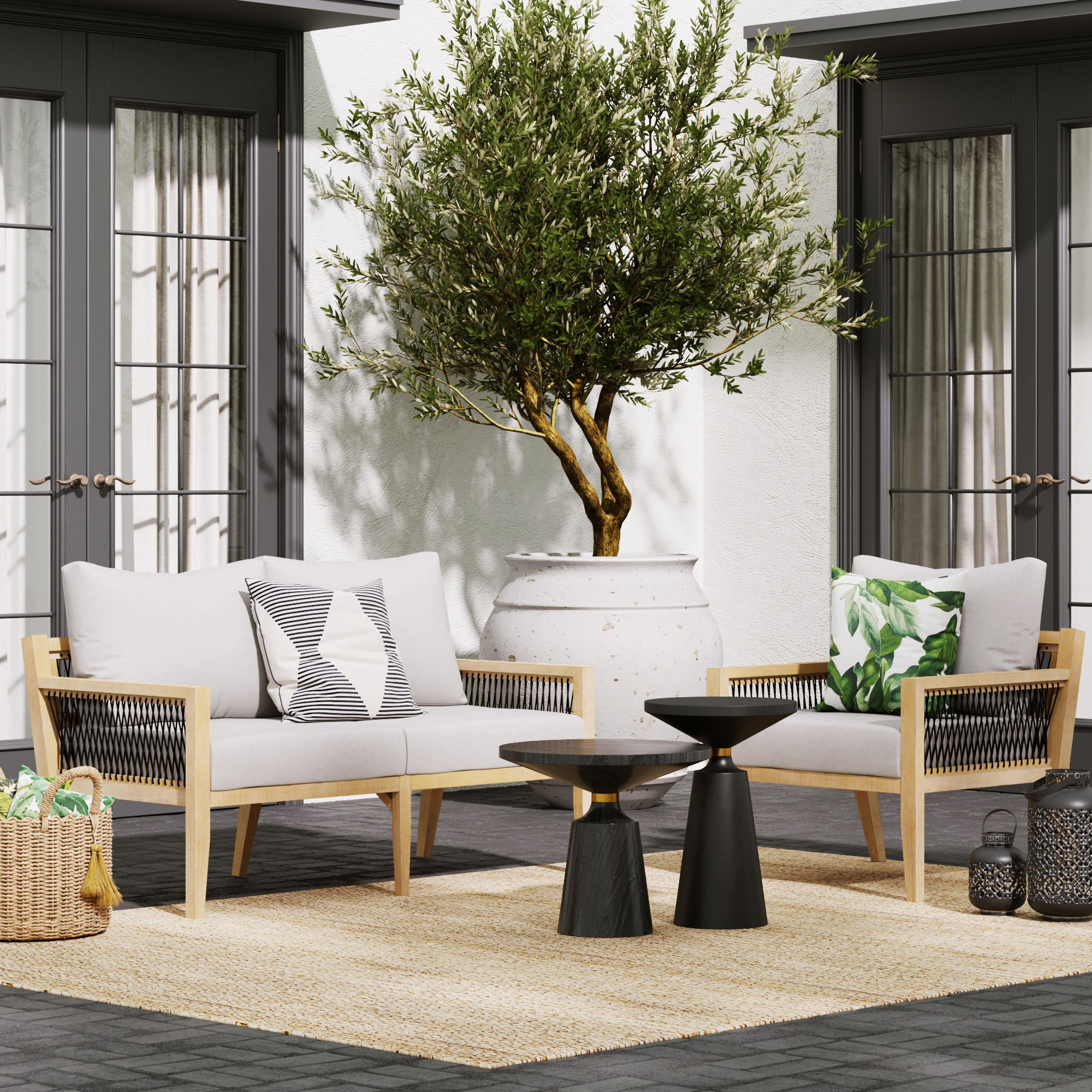 A modern patio features weather-resistant seating: two light gray chairs, a matching Nathan James Outdoor Solid Wood Patio Loveseat Gray Acacia, black tables, a large potted tree, woven rug, throw pillows, and a wicker basket by double glass doors.