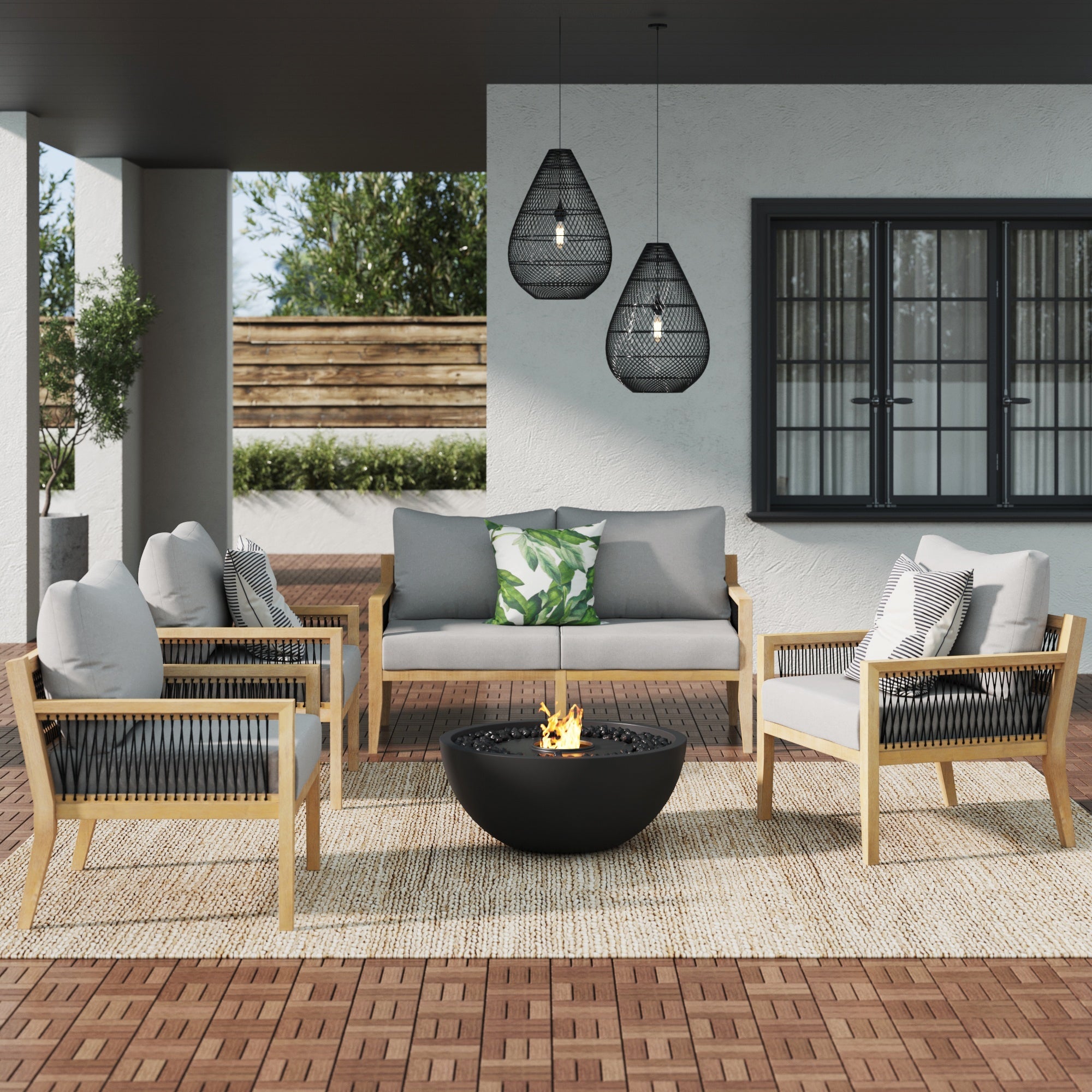 Modern patio with the Nathan James Outdoor 4 Piece Wood Patio Chair Set, featuring weatherproof acacia frames, gray cushions, a round black fire pit, patterned pillows, and pendant lights on a green-lined sheltered deck.