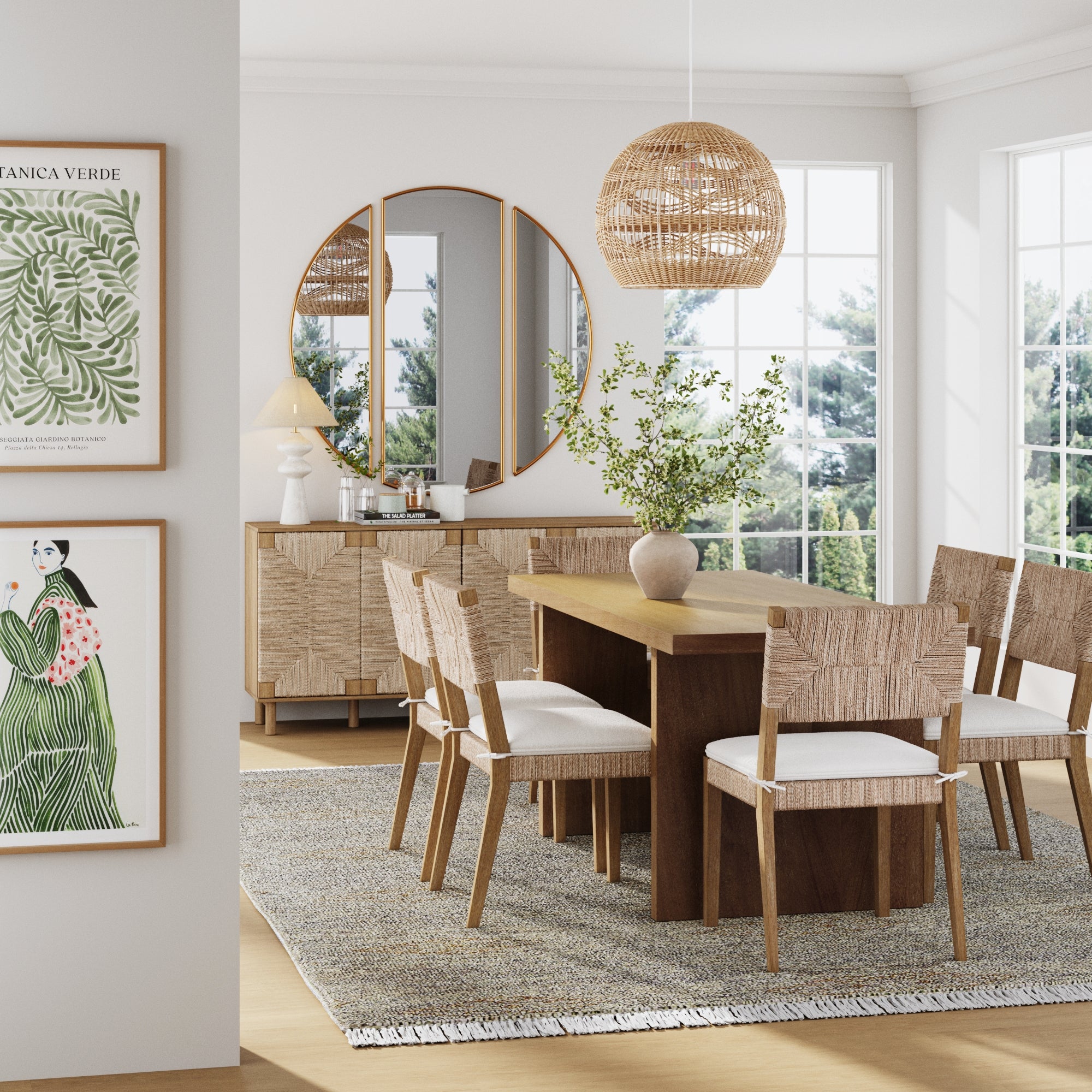 A bright, modern dining room with a solid wood table, six Nathan James Boucle & Seagrass Dining Chairs in light brown, a gray rug, and greenery in a vase. Large windows, botanical art, a round mirror, and a wicker pendant add the finishing touch.