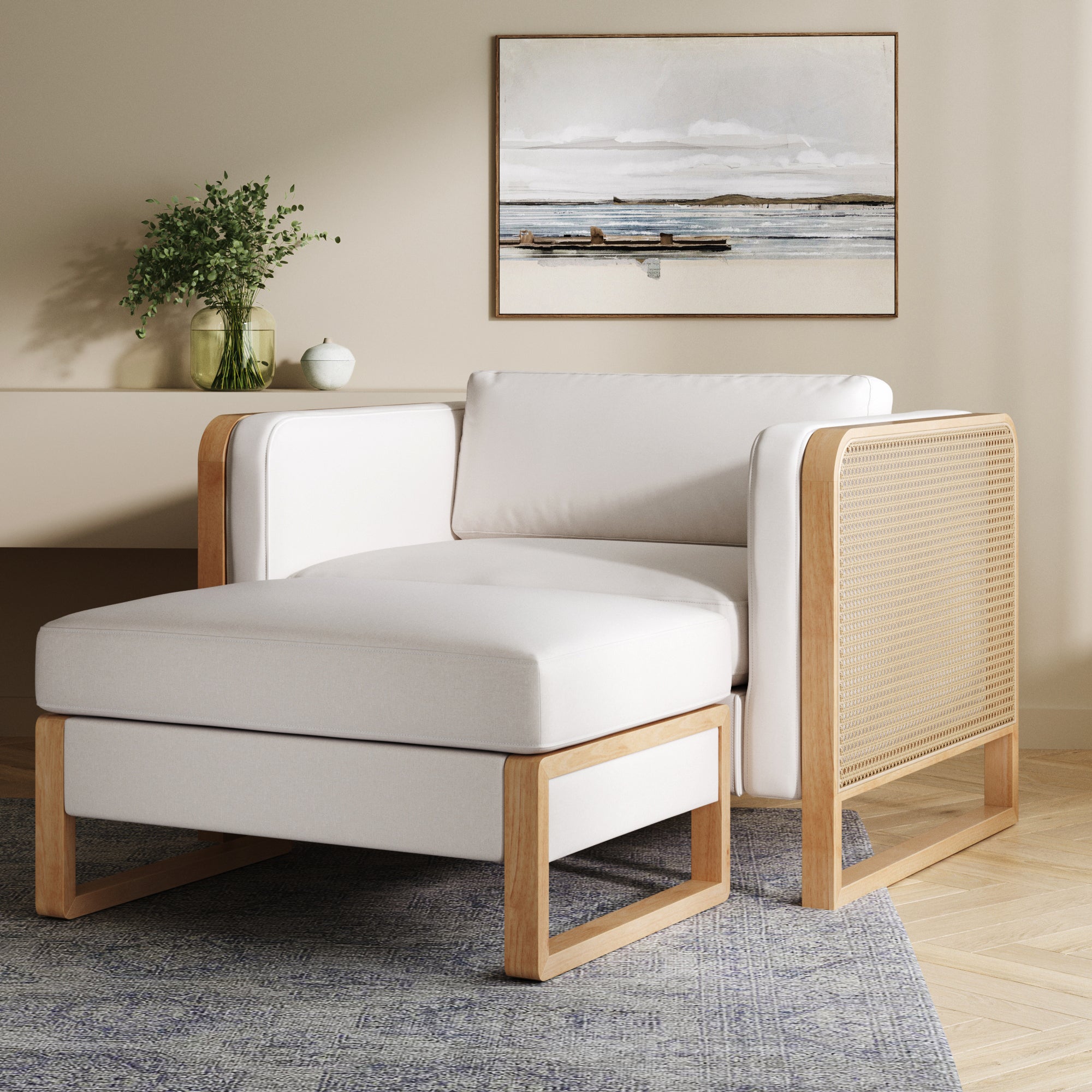 The Nathan James Solid Wood Rattan Accent Chair with Ottoman Set in Bisque, featuring white cushions and a woven side panel, sits atop a blue rug in a neutral room beneath boat artwork above a console table with vases.