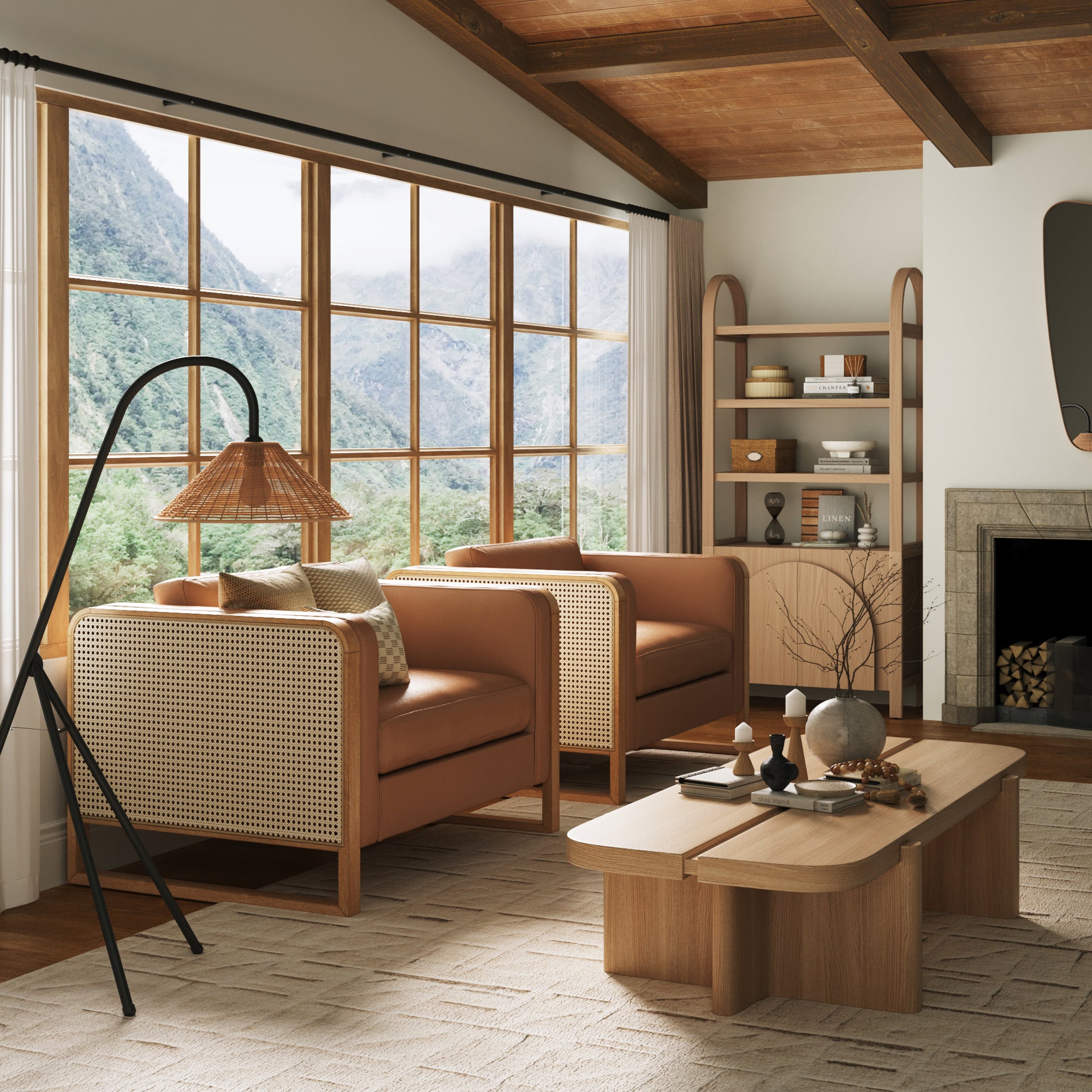 A cozy living room with two rattan armchairs, a wooden coffee table with decor, a modern floor lamp, a fireplace, and large windows showing mountains and trees outside. Shelves with books and ceramics are against the wall.