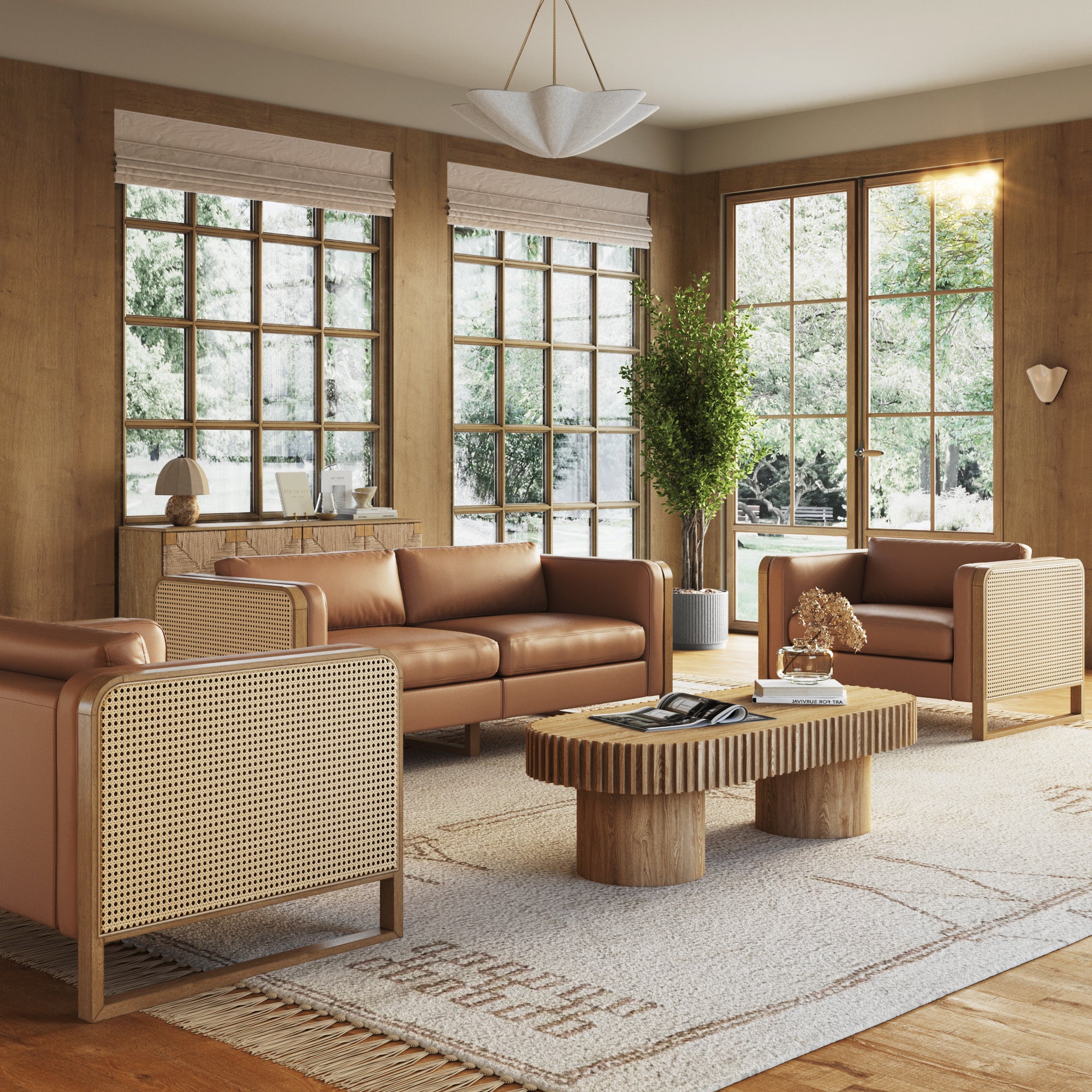 A cozy living room featuring the Nathan James Solid Wood Accent Chair with Rattan Arm Camel (Set of 2), a modular sofa, patterned rug, coffee table, large windows, indoor plants, and neutral-toned decor bathed in natural sunlight.