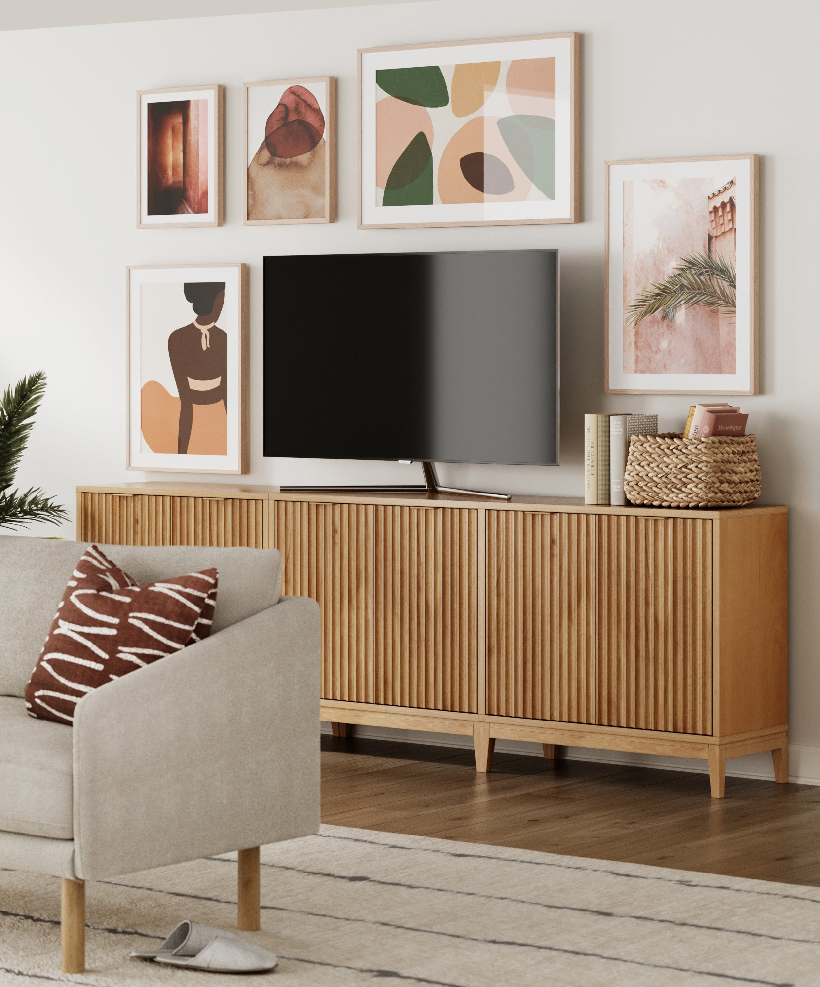A modern living room with a light wood TV console, a flat-screen TV, framed abstract and nature art on the wall, a gray sofa with a brown patterned pillow, and a woven basket on the console.