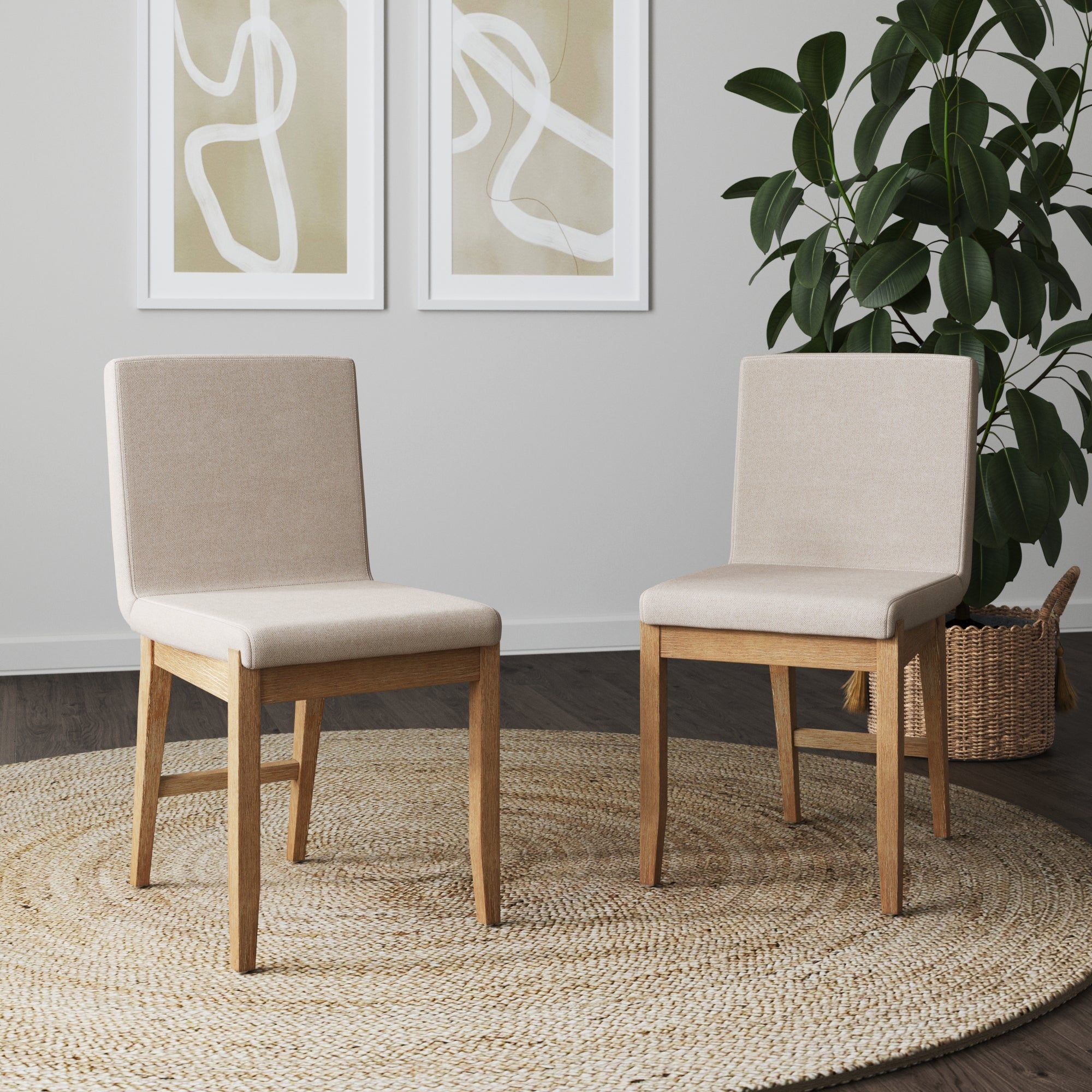 Two Nathan James Dining Chair Light Brown Flax (Set of 2) are arranged on a round woven rug in a modern room, with a large potted plant and two abstract white-framed art pieces enhancing the space and complementing the dark wood floors.