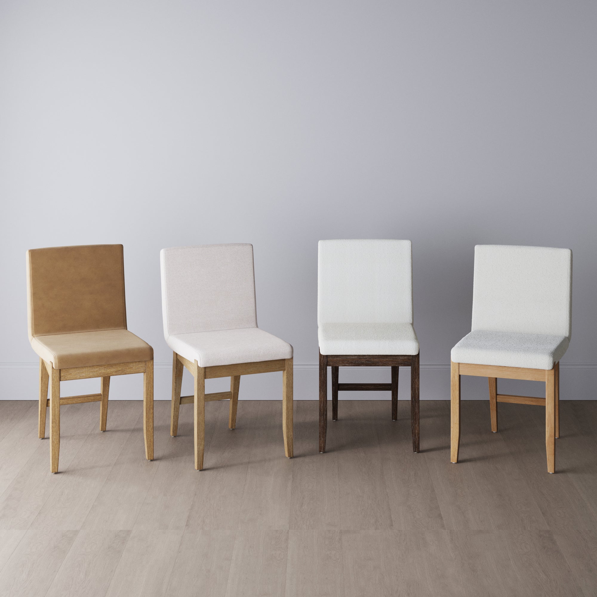 Four upholstered dining chairs in different shades of beige and white are arranged side by side on a light wooden floor against a plain, light gray wall.