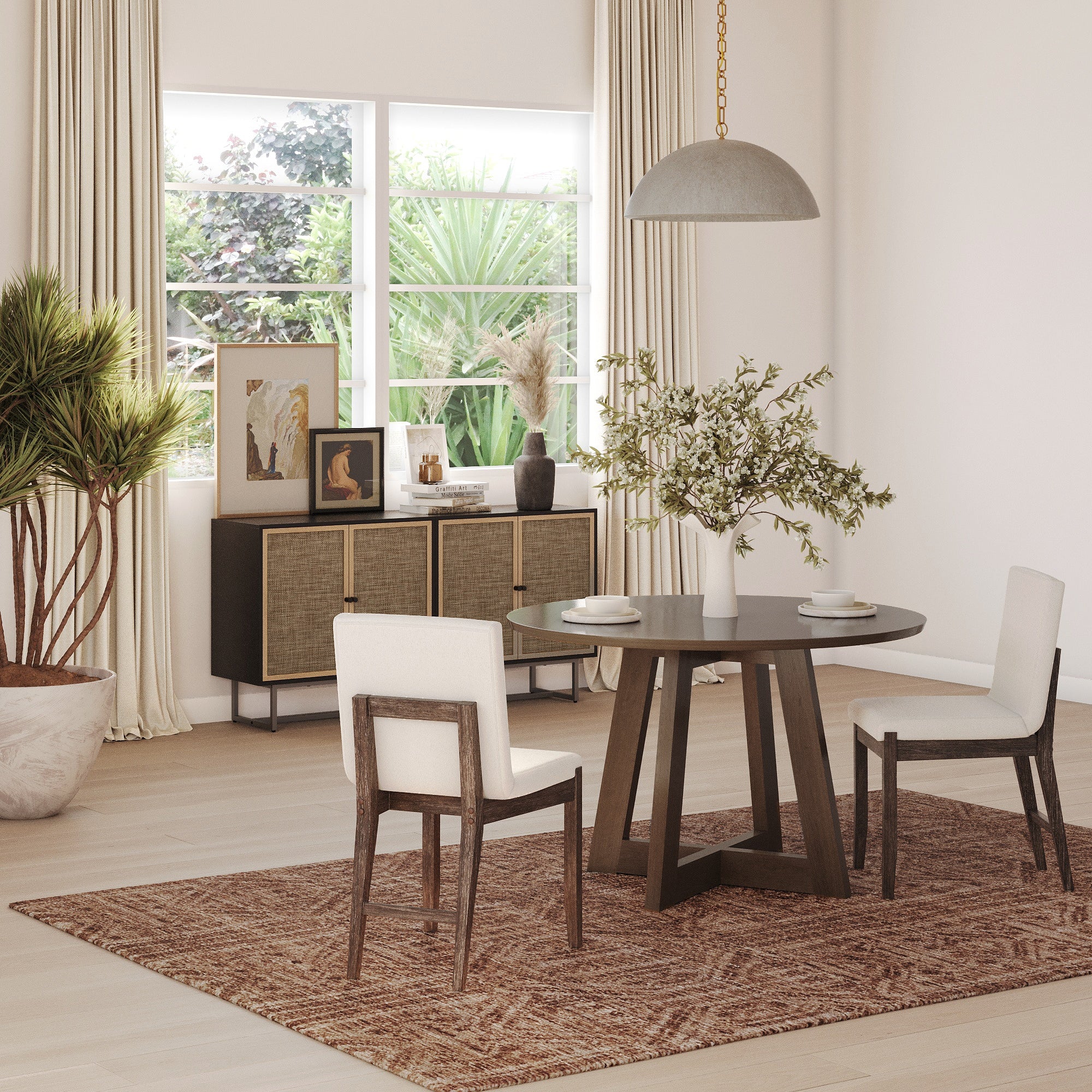 A modern dining room with a round dark wood table, three Nathan James Exposed Back Dining Chairs in dark brown, a woven rug, large window, sideboard with art and decor, potted plants, and a hanging pendant light filled with natural light.