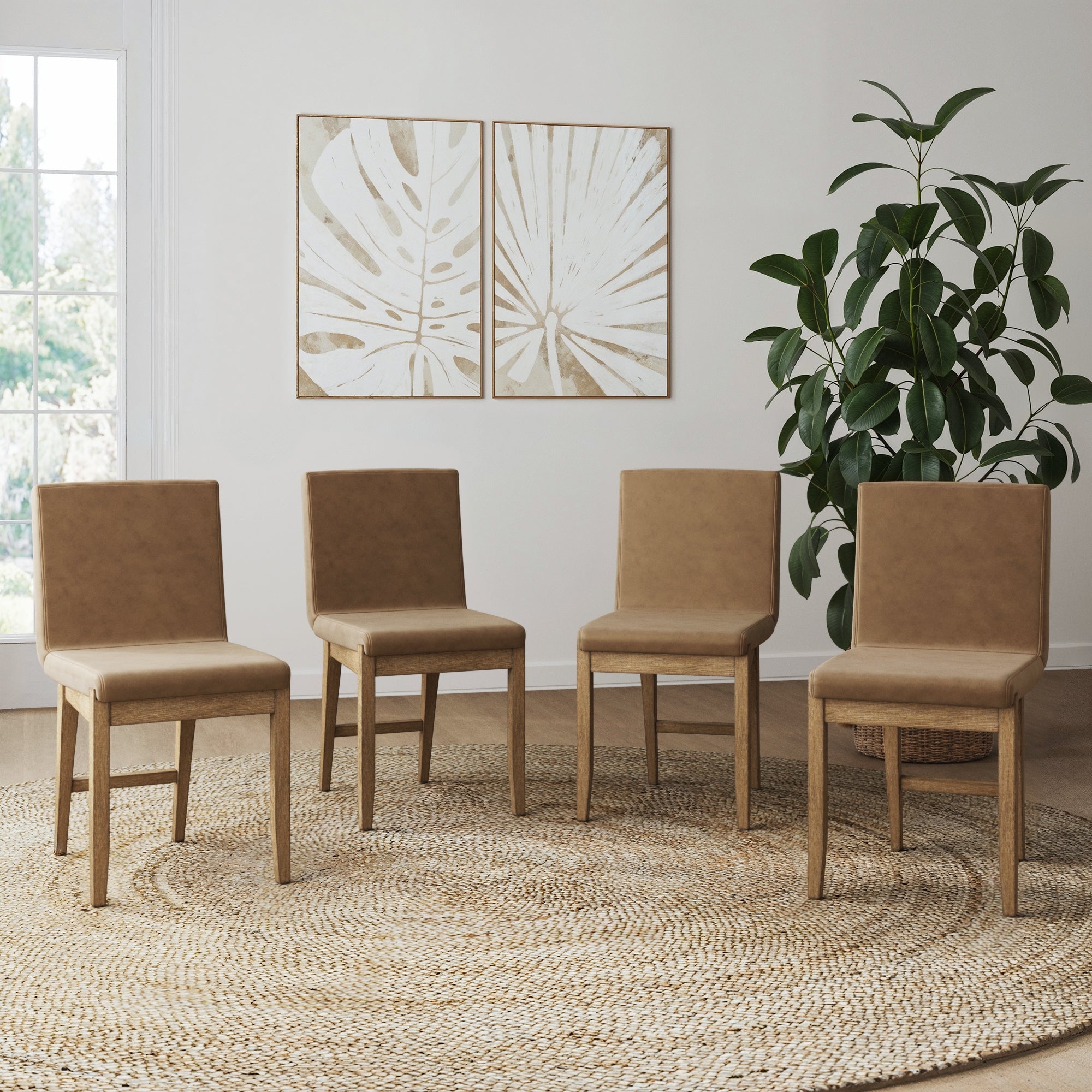Four Nathan James Exposed Back Dining Chairs Light Brown (Set of 4) are arranged on a woven rug in a bright room with large windows, a potted plant, and two abstract leaf artworks on the wall.