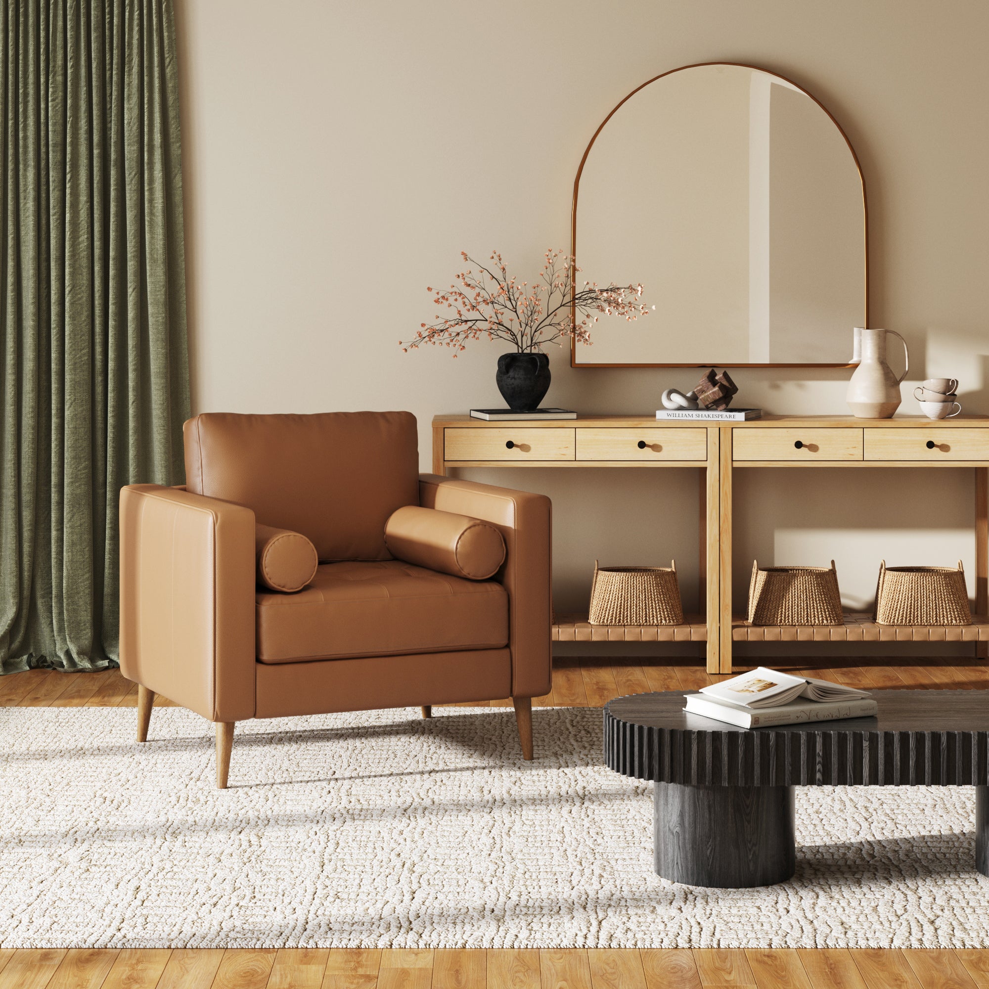 A modern living room featuring the Nathan James Mid-Century Tufted Leather Armchair in camel, a wooden console with baskets, a large arched mirror, decorative vases, black oval coffee table, green curtains, and a textured white rug.