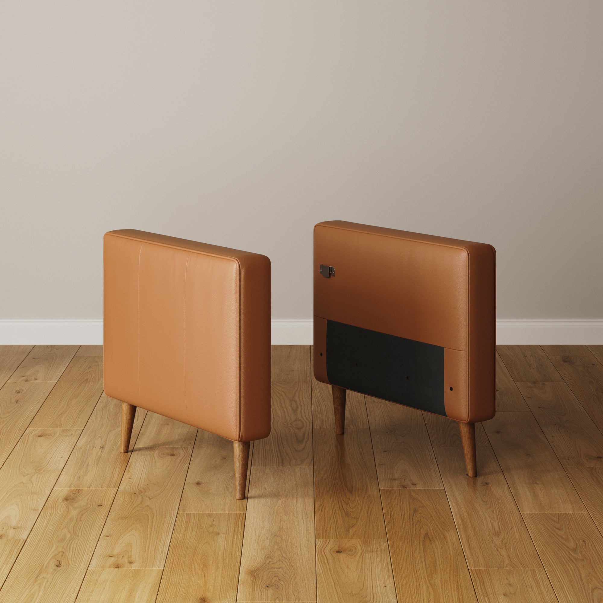Two tan, rectangular cushioned heaters with wooden legs sit on a light wood floor by a beige wall, complementing the Nathan James Mid-Century Tufted Leather Sofa Standard Arm Camel (Modular Sofa Part). One heater faces front; the other shows its black panel and knob.
