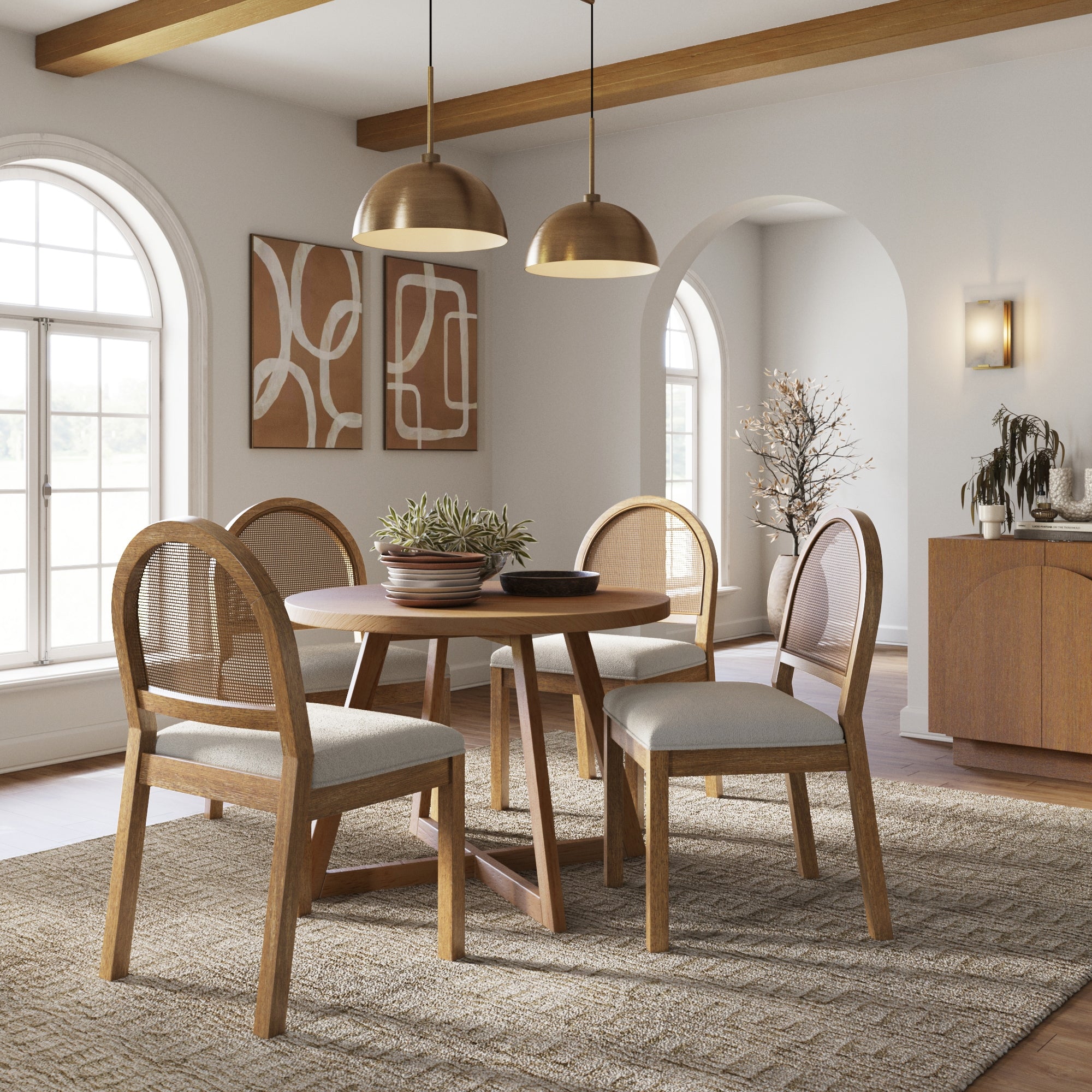 A cozy dining room with a round wooden table, four cushioned chairs, two gold pendant lights, abstract wall art, arched windows, and neutral decor, including a sideboard and a plant.