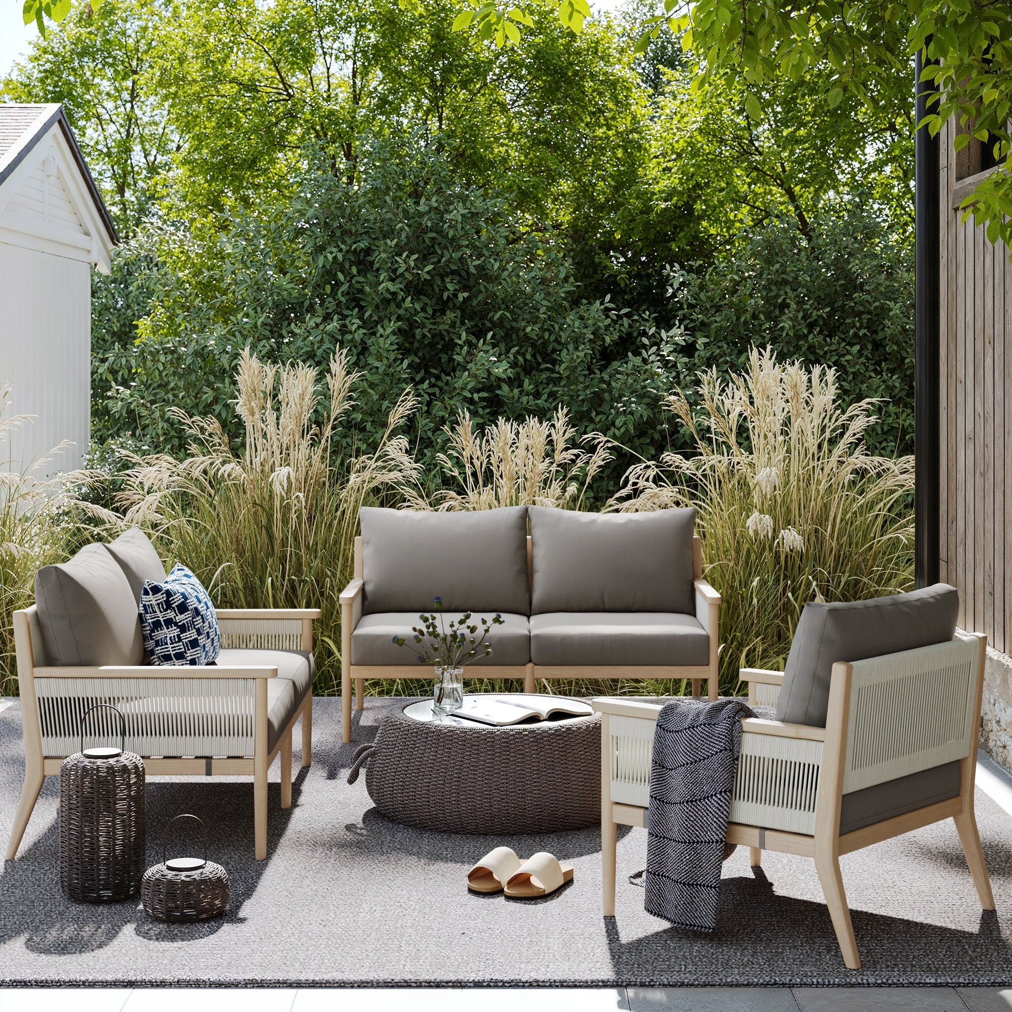 Create a cozy modern patio with the Nathan James Outdoor Wood & Rope Patio Loveseat in medium gray, featuring weatherproof acacia wood, washable gray cushions, and woven accents—perfect for relaxing among tall grasses and decor.