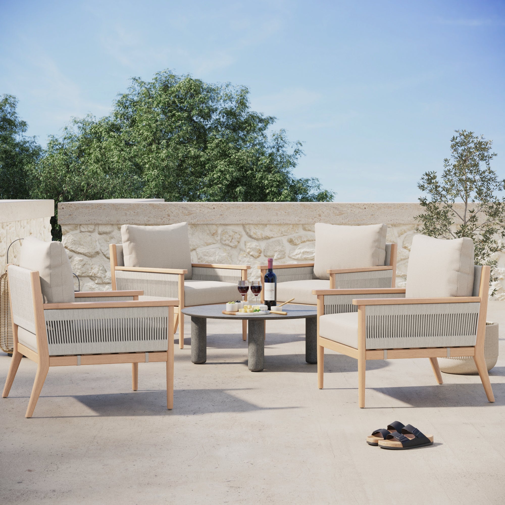 Four Nathan James Outdoor Wood & Rope Patio Arm Chairs in Ash White circle a low round table with wine and snacks. Weatherproof acacia wood and washable covers combine style and practicality for any patio.