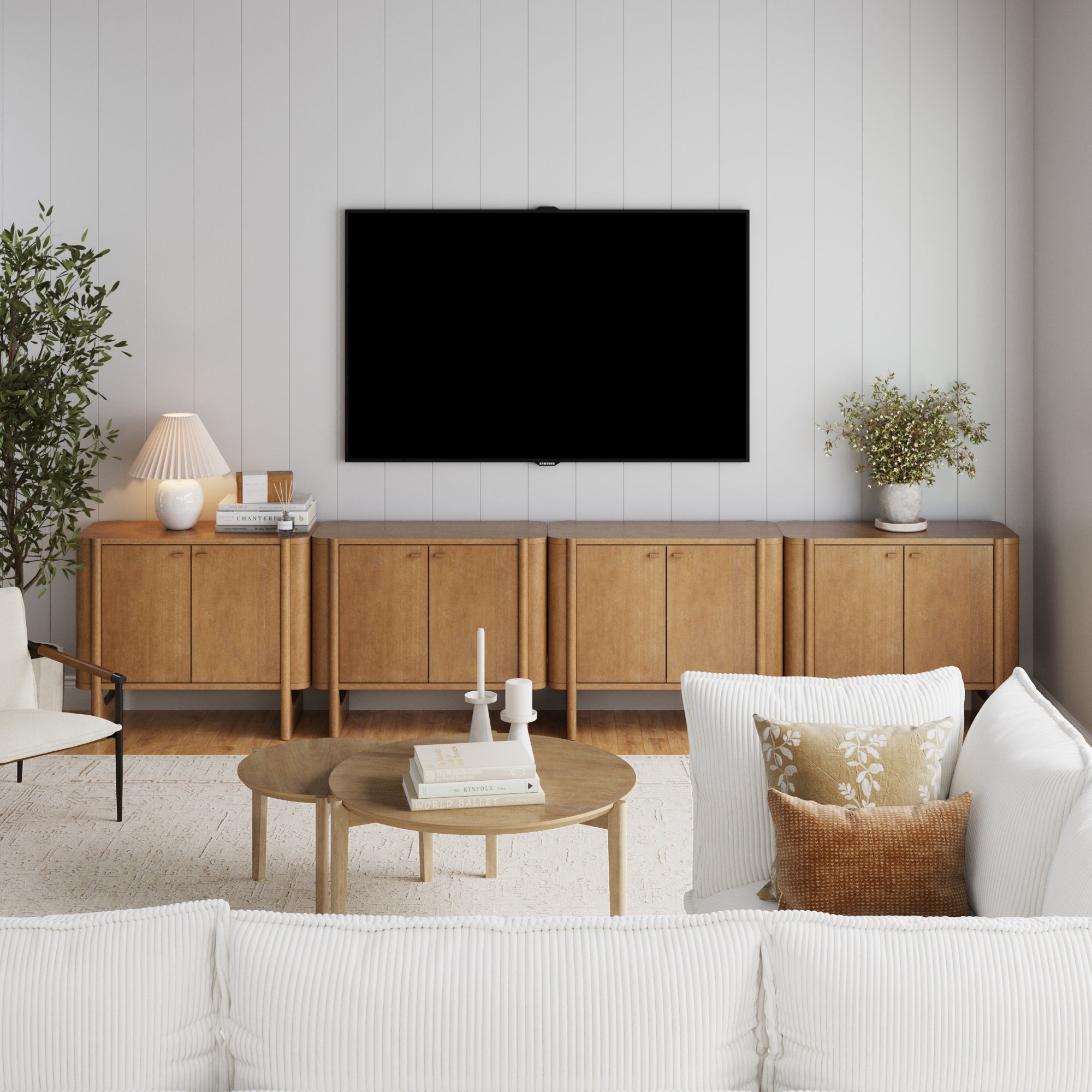 A modern living room showcases a wall-mounted TV above the Nathan James Mid-Century Modern Solid Wood Credenza TV Stand (Set of 4), a white sofa with patterned pillows, a wooden coffee table, potted plants, and decorative accents.