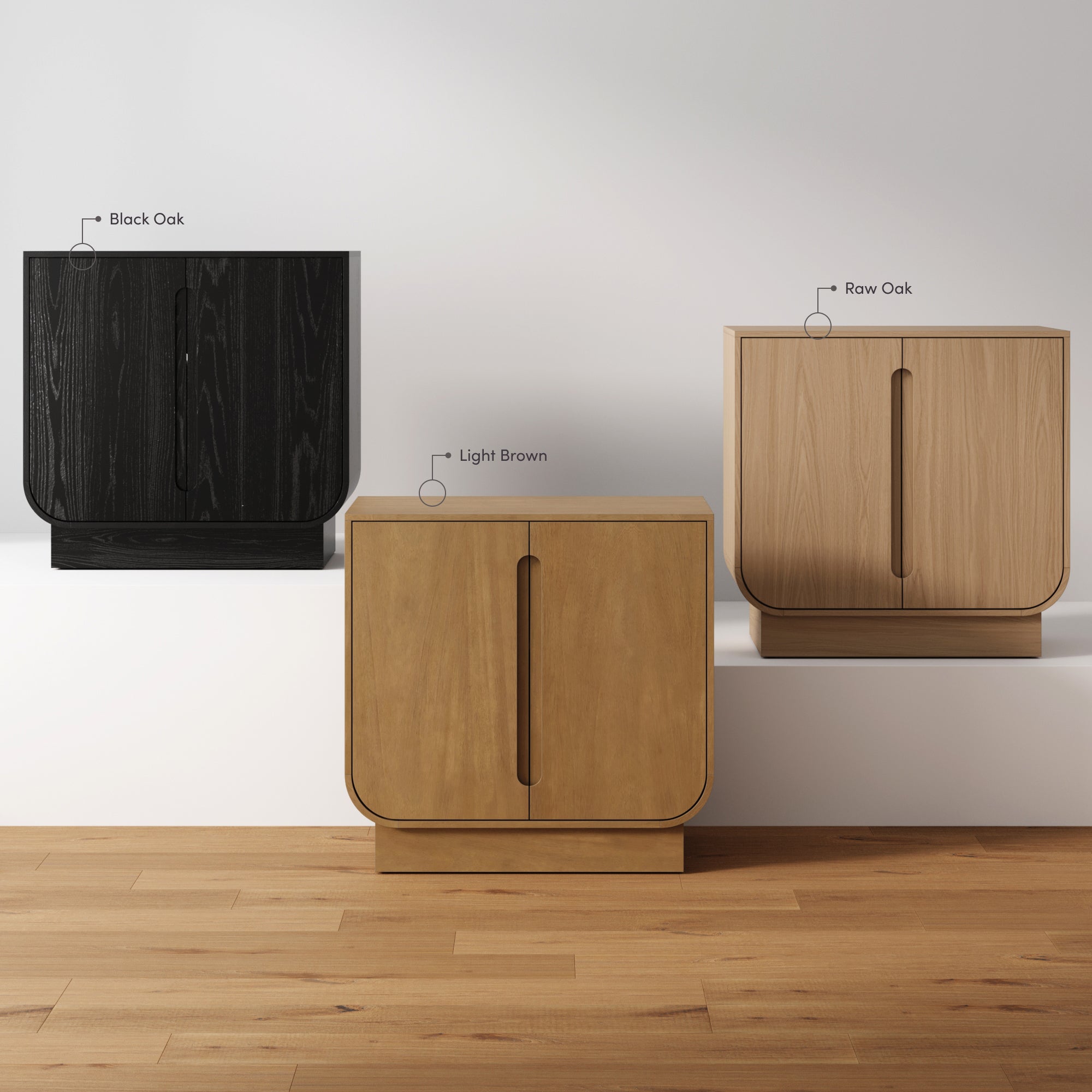 Three modern cabinets in different finishes—black oak, light brown, and raw oak—are displayed side by side on a wooden floor against a white wall. Each cabinet has a vertical groove handle.