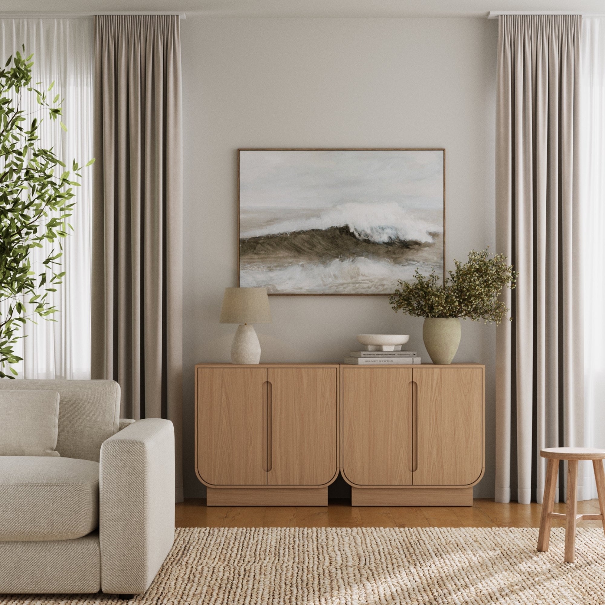 A modern living room with beige curtains, a light sofa, tan woven rug, vases, a lamp, and two Nathan James Veneer Arched Accent Cabinets in Raw Oak used as storage beneath a framed waves painting.