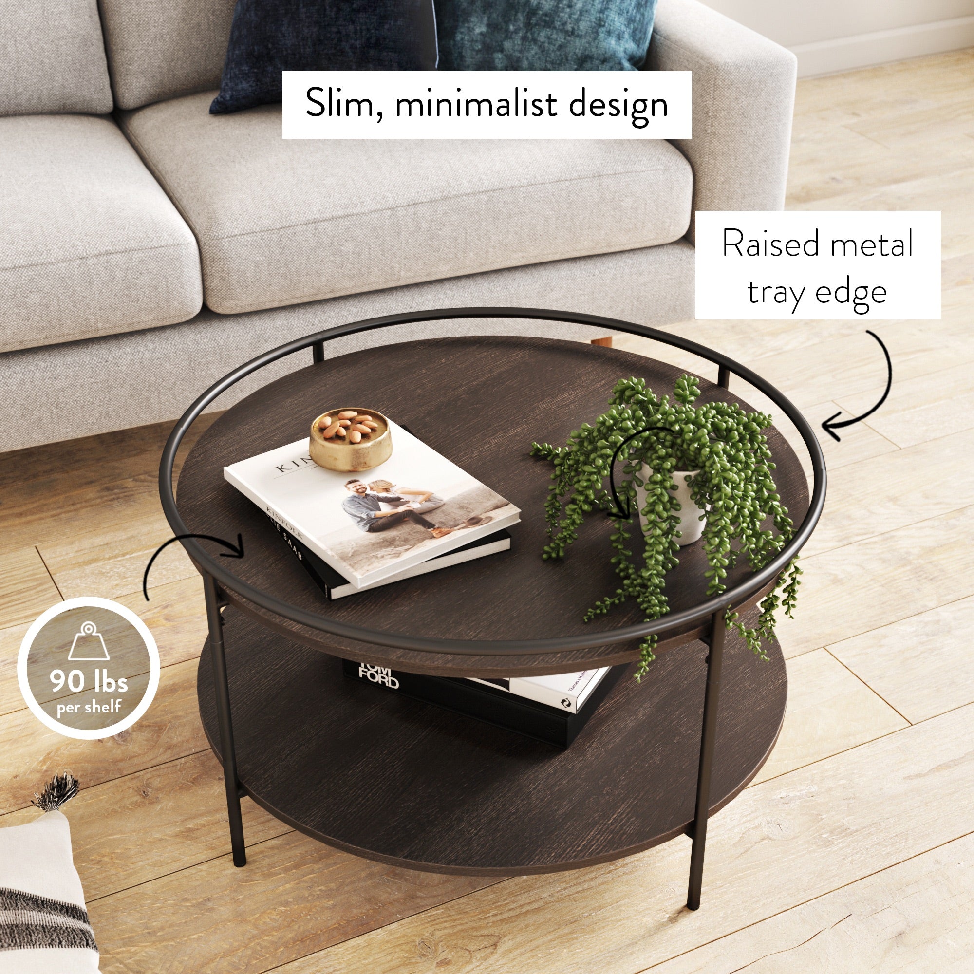 Round, dark wood coffee table with a raised metal tray edge, two shelves, and slim minimalist design. Decor includes books, a bowl, and a potted plant. Text highlights features and a 90 lbs per shelf weight limit.