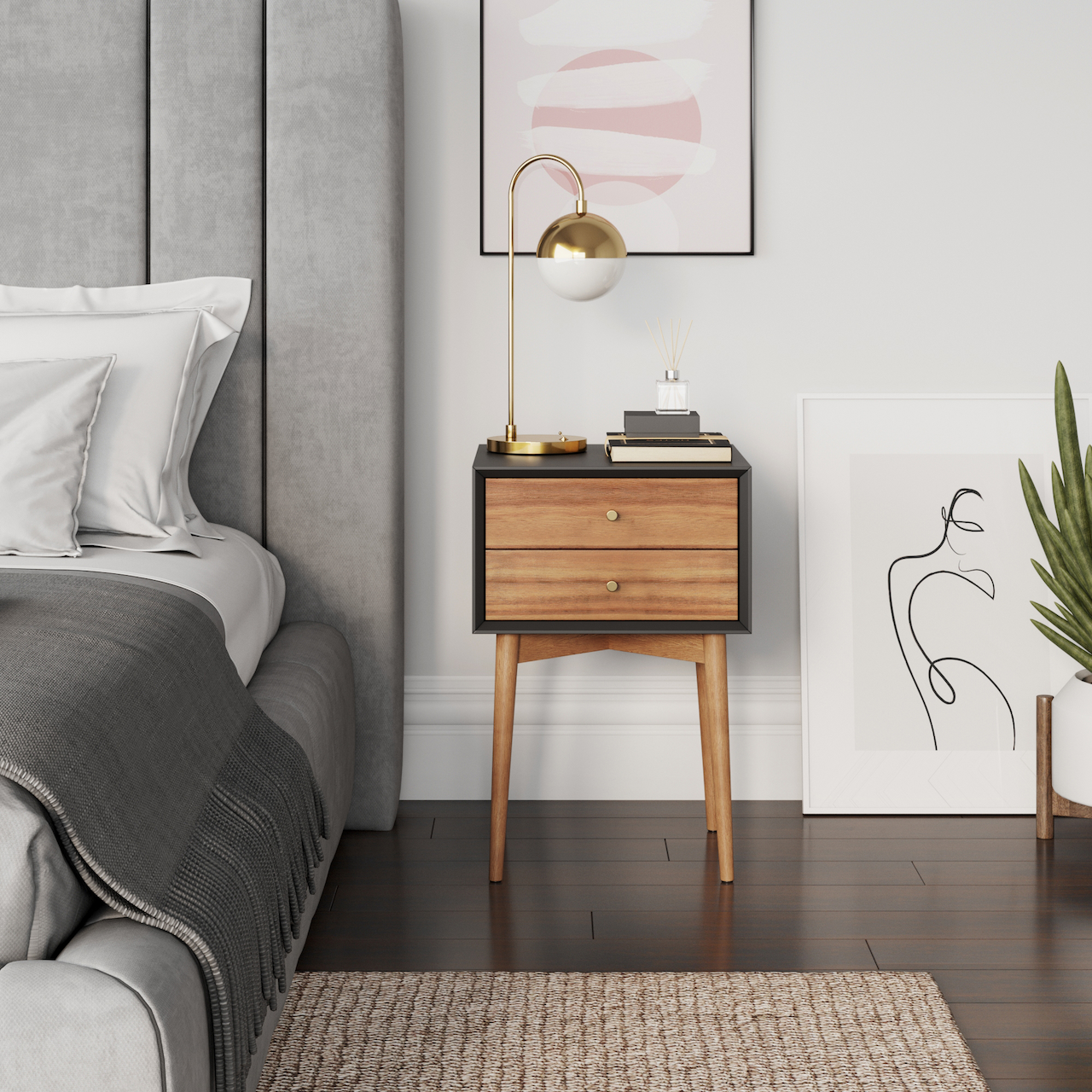 A modern bedroom features a gray upholstered bed, a wooden nightstand with a gold lamp, abstract art on the wall, a framed minimalist line drawing on the floor, a green plant, and a woven rug on dark wood flooring.