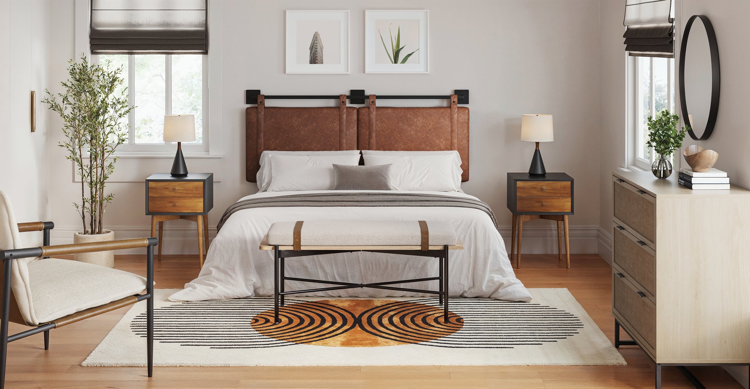Modern bedroom with a leather headboard, neutral bedding, wooden nightstands with lamps, a bench at the beds foot, a dresser, two framed prints, and a white rug with a black and orange geometric pattern.