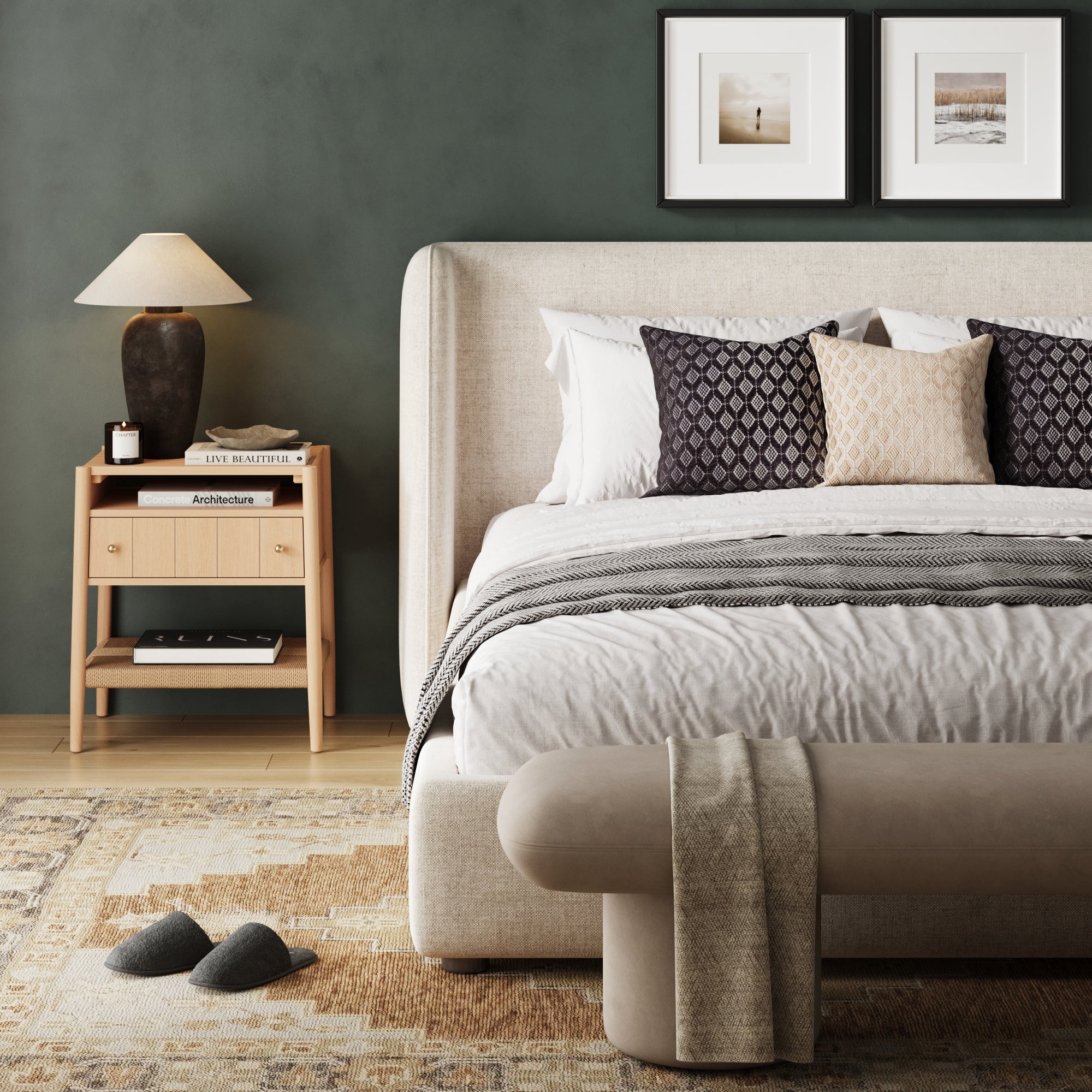 A modern, cozy bedroom with a beige upholstered bed, patterned pillows, framed art on a green wall, rug, slippers, and a Nathan James Wood Nightstand with Drawer & Seagrass Storage in Raw Oak topped with a lamp and decor, plus a cushioned bench with throw.
