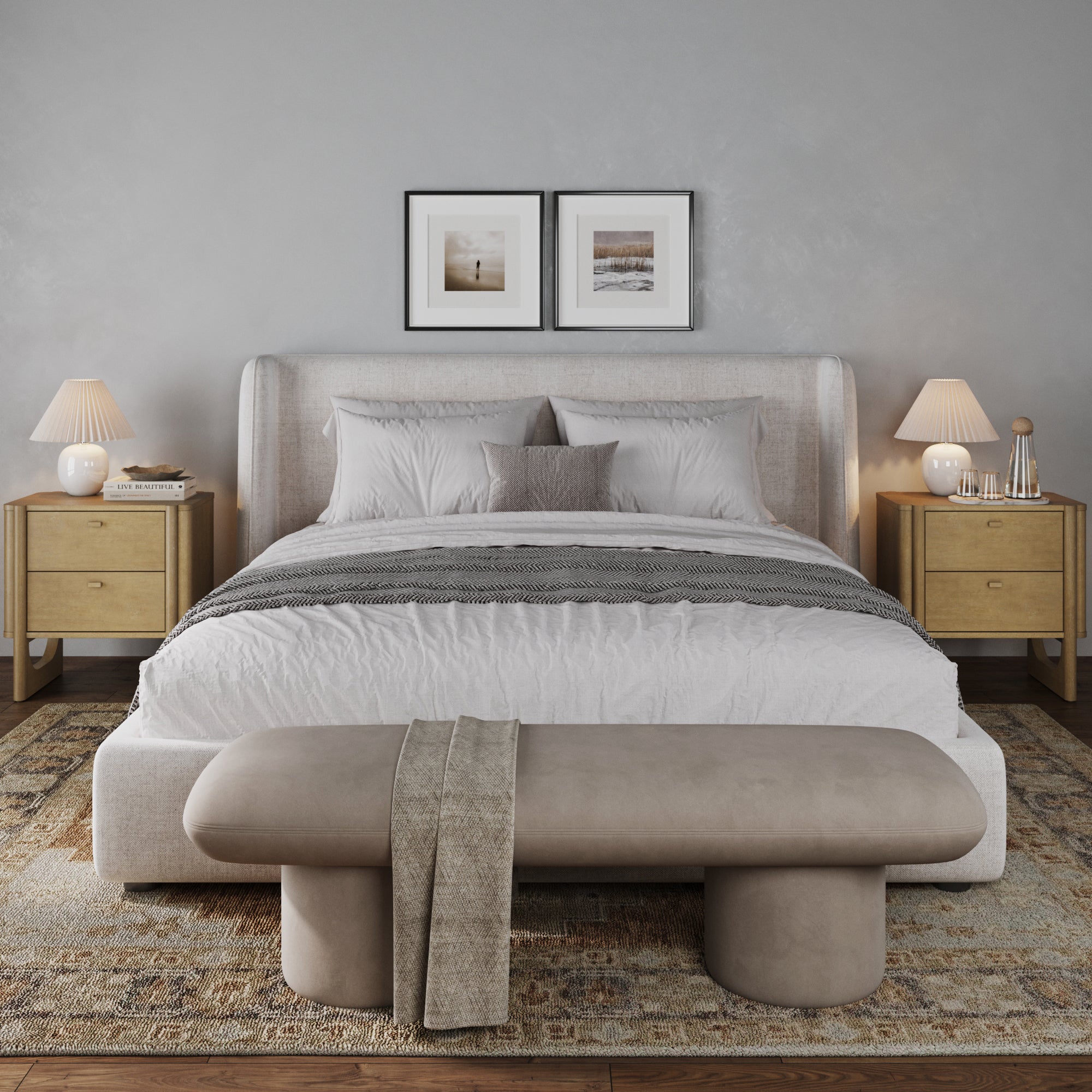 A modern, cozy bedroom with a light upholstered bed, layered pillows, and a gray throw. Two wooden nightstands with lamps and decor flank the bed. A beige bench is at the foot, and neutral artwork hangs above the headboard.