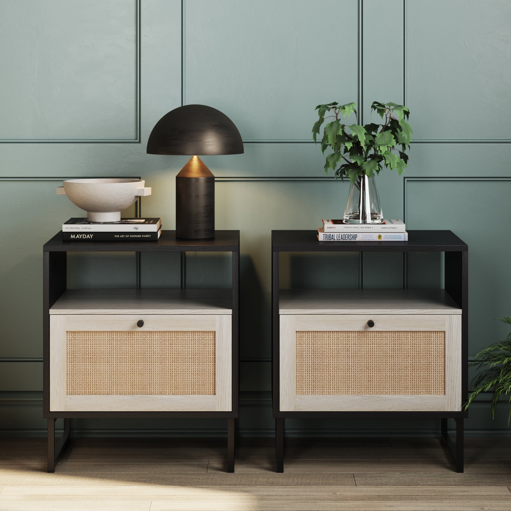 The Nathan James Rattan & Wood Nightstands Black (Set of 2) feature light wood drawers and black frames, placed against a green paneled wall, styled with a lamp, bowl, plant, and books—ideal small space furniture on a light wood floor.