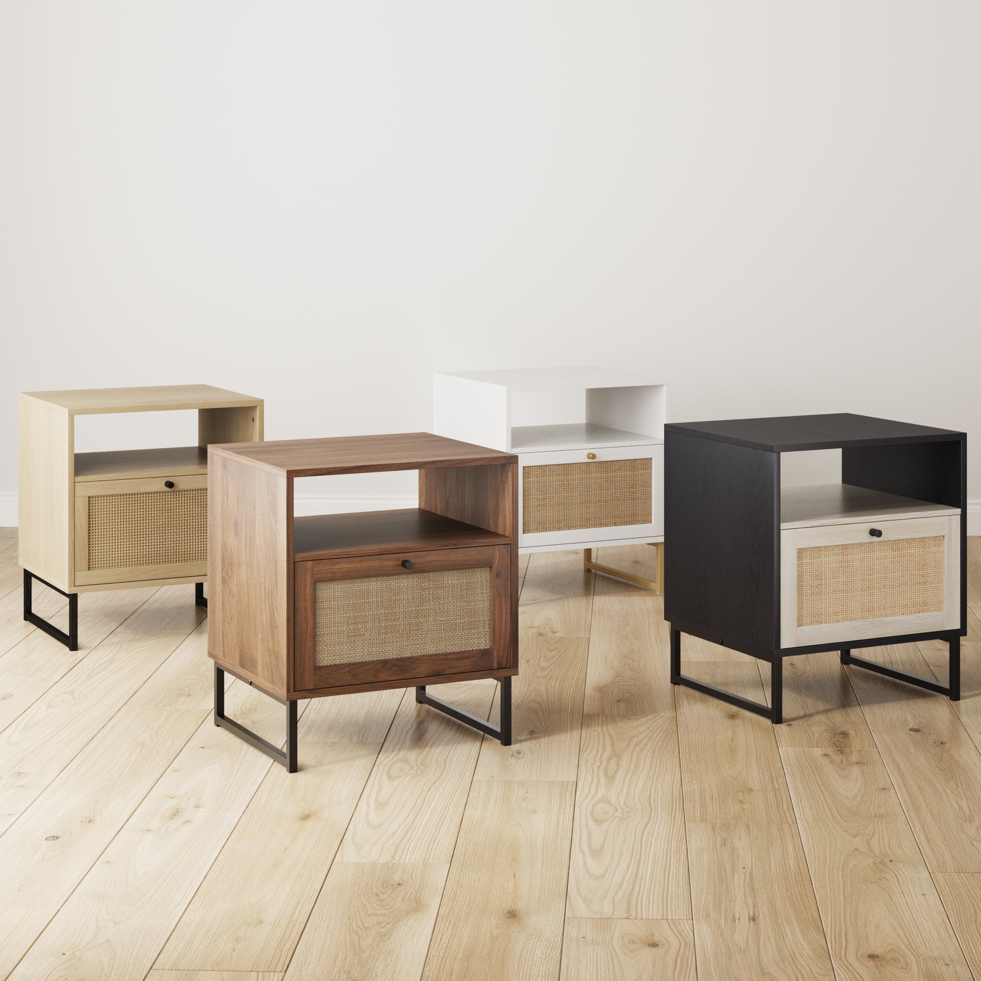Four modern nightstands in different finishes—light wood, walnut, white, and black—each with a drawer featuring a woven rattan front and metal legs, are displayed on a light wooden floor against a plain white wall.
