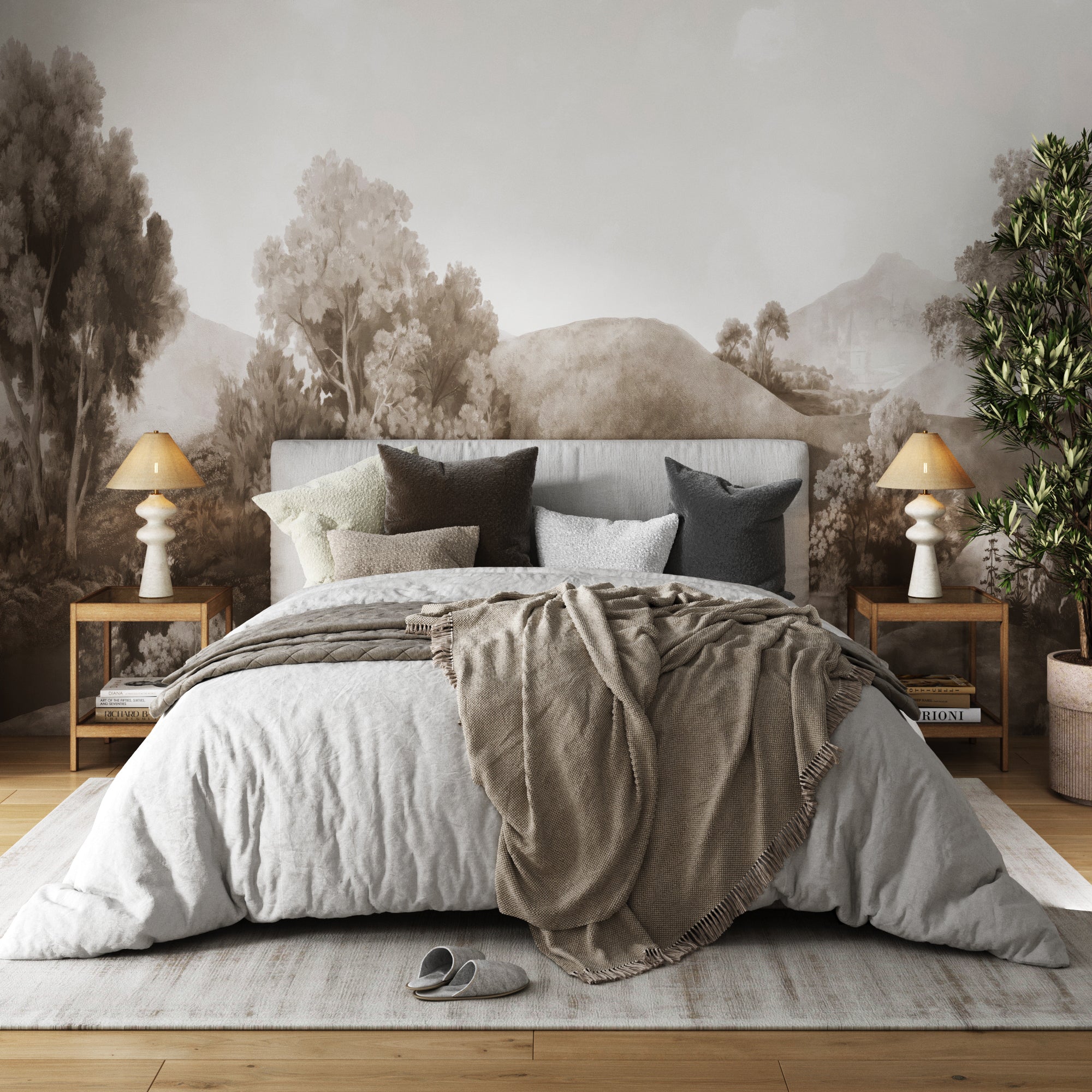 A cozy bedroom with a large bed, layered pillows, and a beige throw. Two Nathan James Solid Wood Rattan & Glass End Tables with lamps sit by a tree-themed mural. A slipper and potted plant rest on the wooden floor.