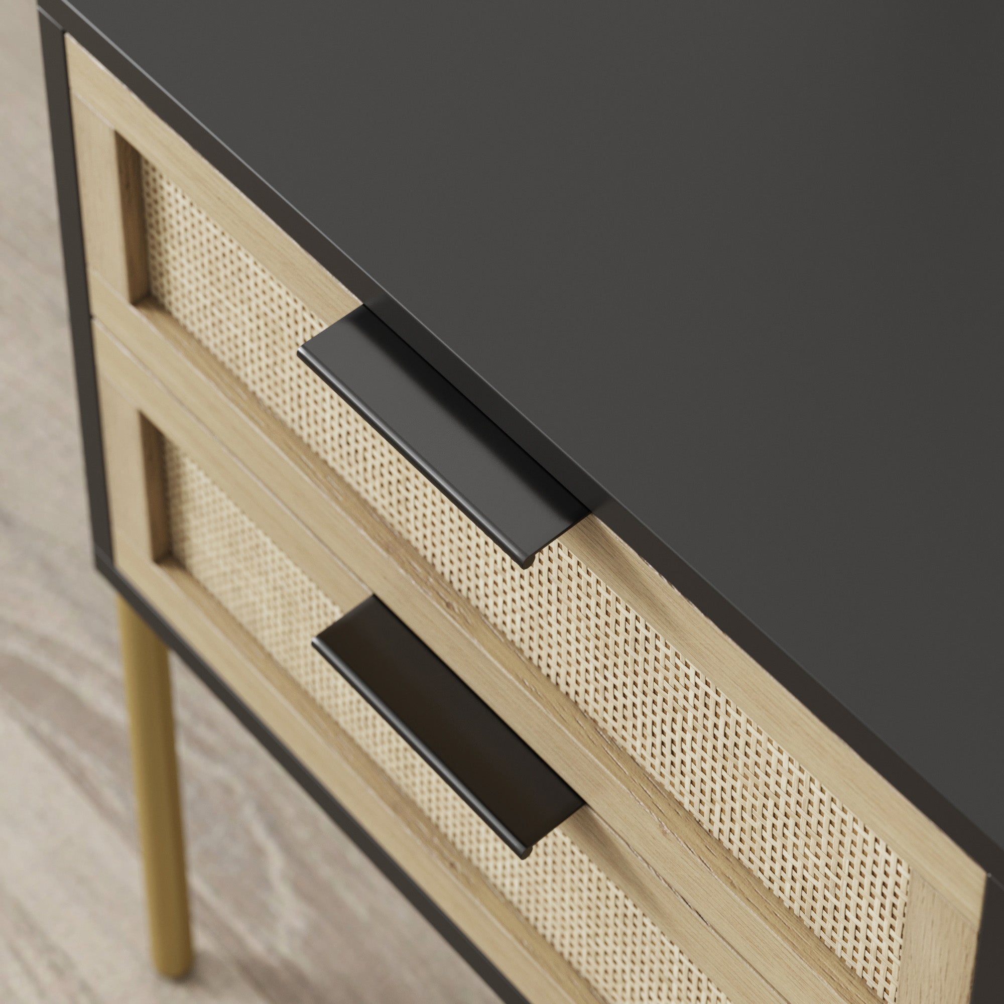 Close-up of a modern wooden dresser with two drawers featuring black handles and woven rattan panels, standing on thin gold legs, on a light wood floor.