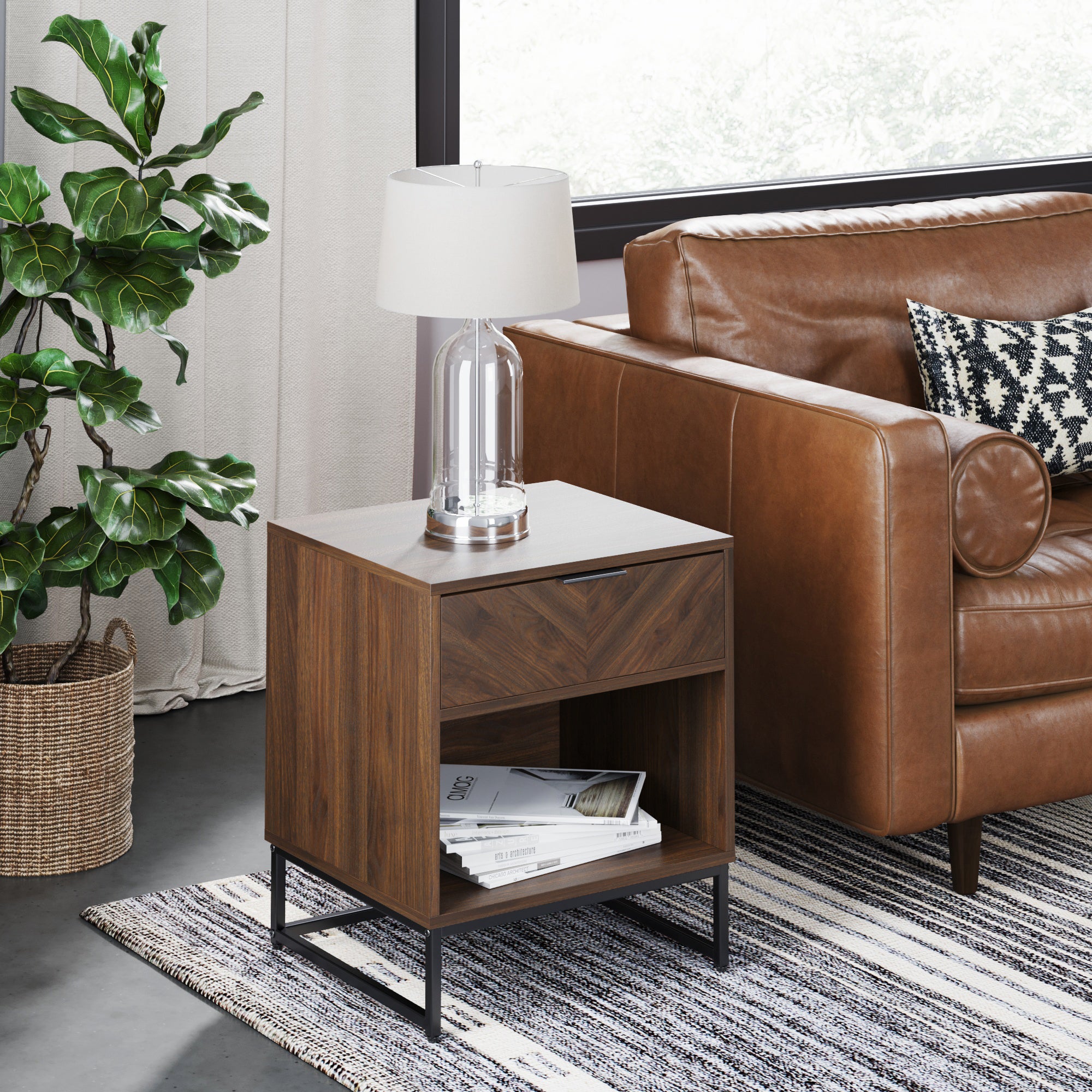 A modern living room with a brown leather sofa, a wooden side table with a drawer and lamp, a striped rug, a potted plant, and a large window with natural light.