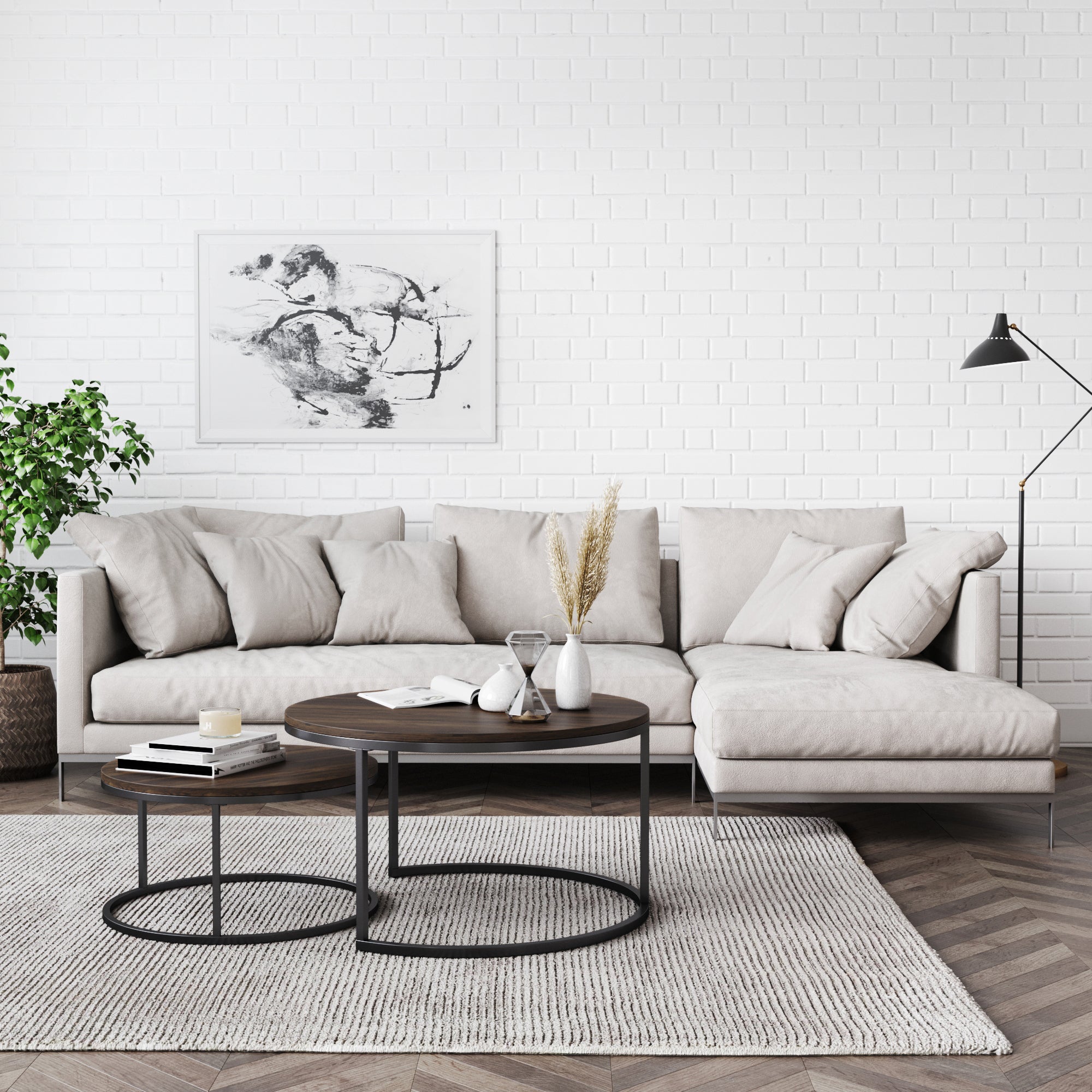 A modern living room with a light beige sectional sofa, round wooden coffee tables, a gray rug, a potted plant, a black floor lamp, and a black-and-white abstract painting on a white brick wall.