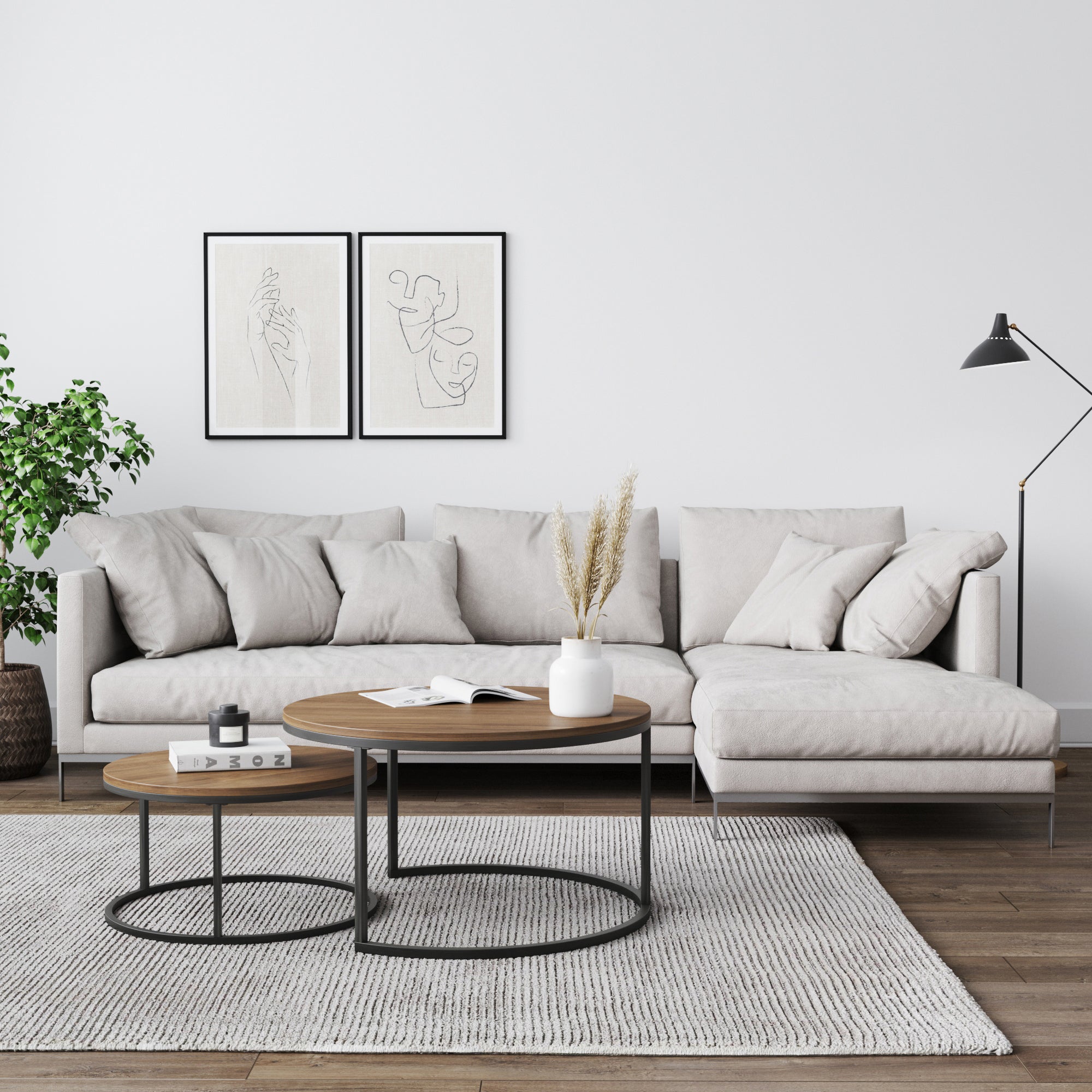 A modern living room with a light gray sectional sofa, two round wooden coffee tables, a white rug, minimalist wall art, a potted plant, and a black floor lamp on hardwood floors.