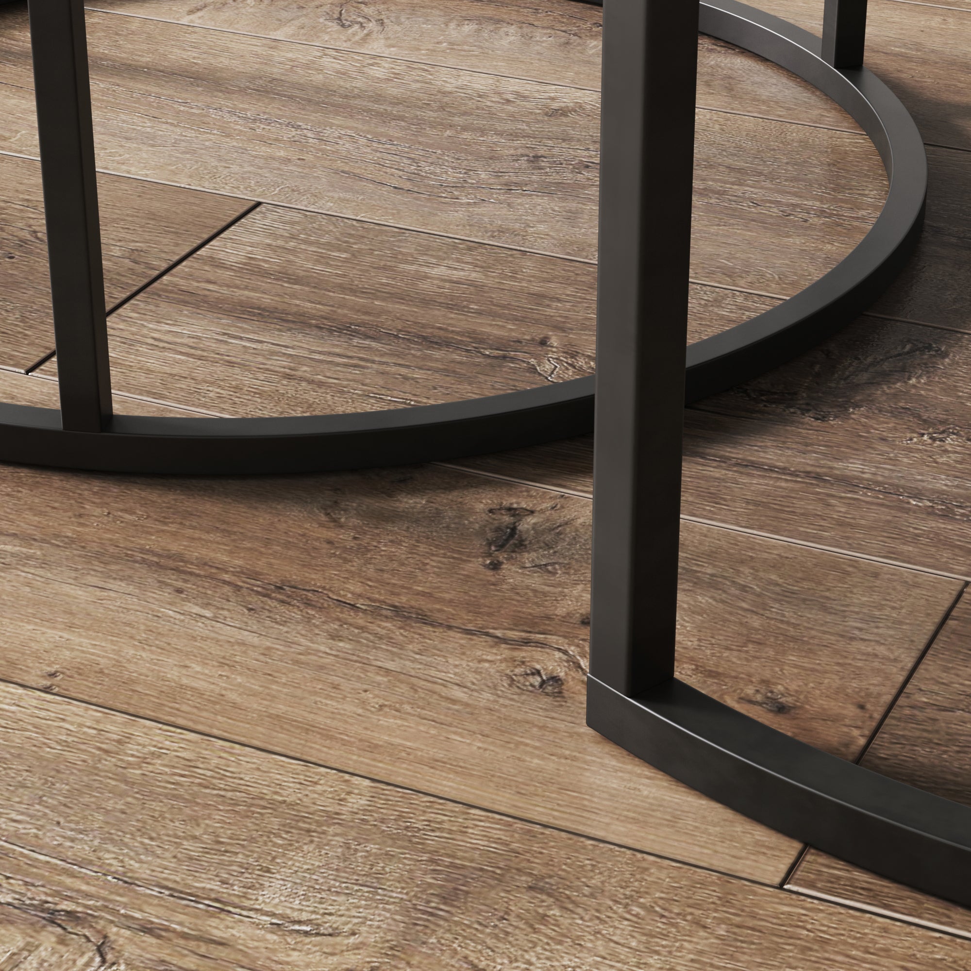 Close-up of black metal legs and circular base of a table or chair on a wooden floor with a natural grain pattern.