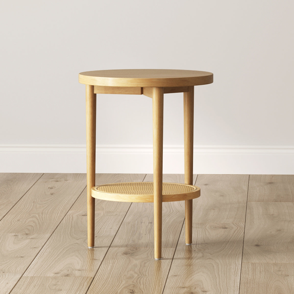 A small, round wooden side table with four legs and a lower shelf, placed on a light wood floor against a plain light-colored wall.