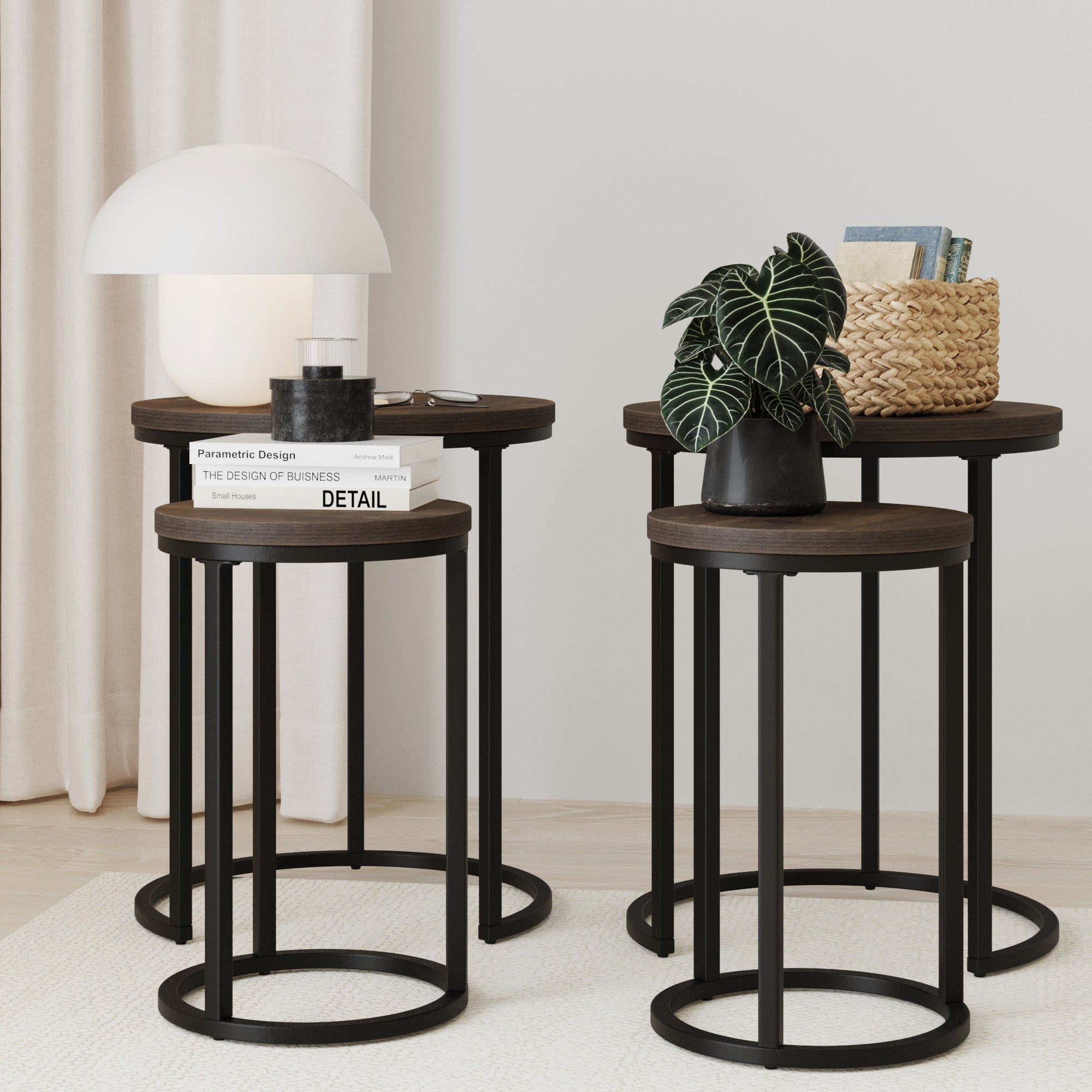 Two Nathan James Nesting Round End Tables in black and nutmeg hold a lamp, books, a potted plant, and a woven basket. The versatile tables are arranged together against light curtains and a pale wall.