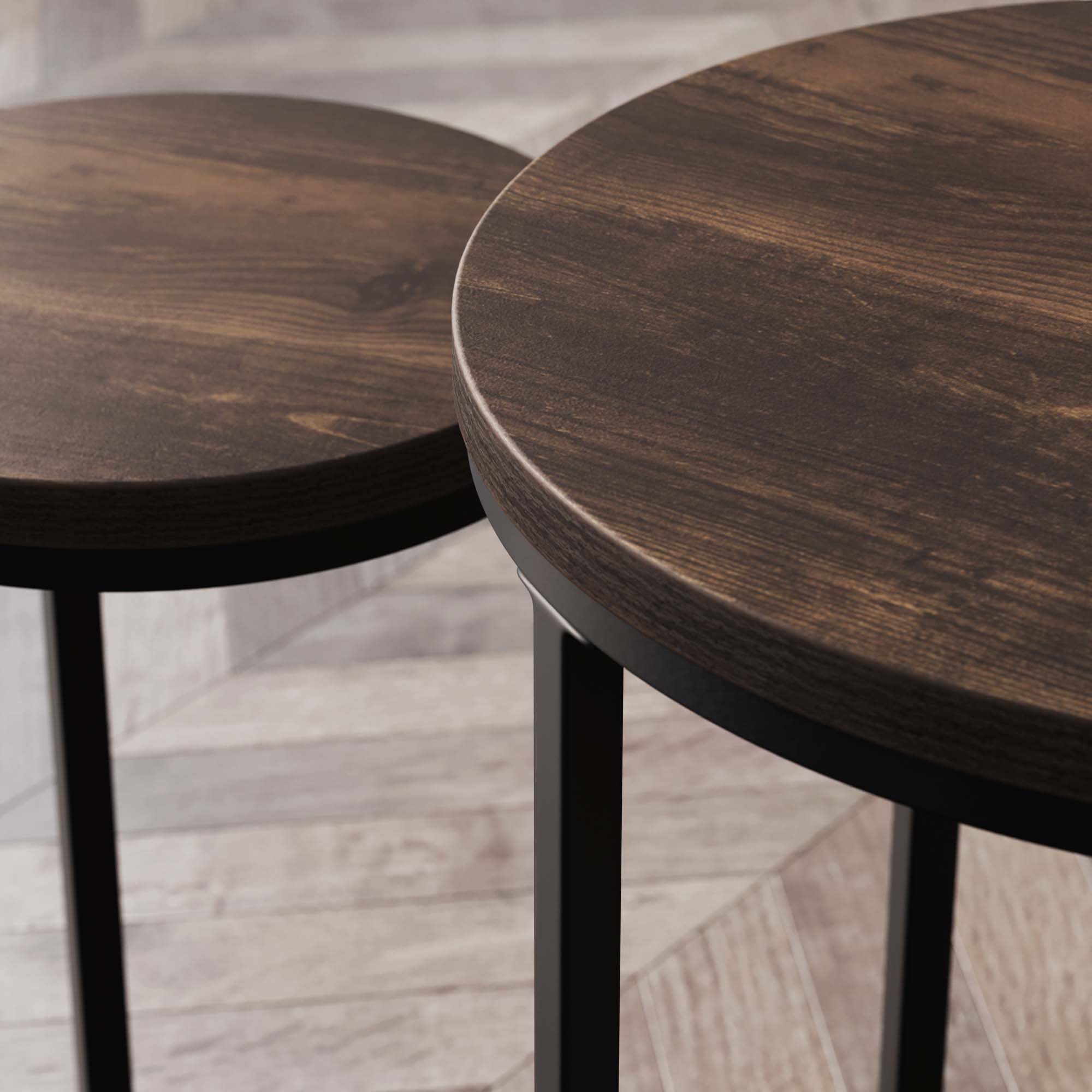 Close-up of two round, dark wooden tabletops with black metal legs, positioned side by side on a light-colored, patterned wooden floor.
