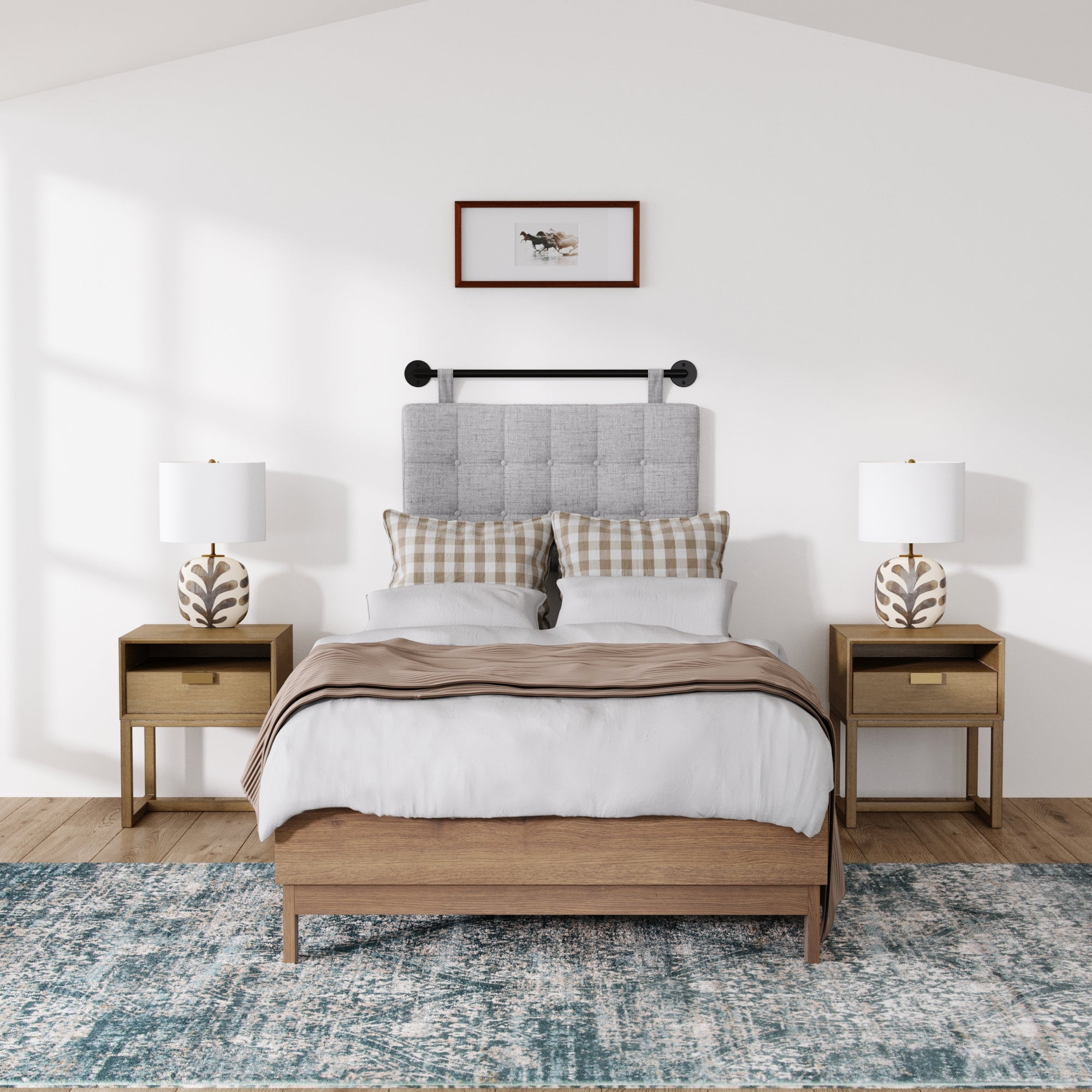 A modern bedroom features a wooden bed with a light gray tufted headboard, white bedding, plaid pillows, and a framed picture above. Two Nathan James Wood Modern Farmhouse Nightstands flank the bed on a blue patterned rug, each topped with a lamp.