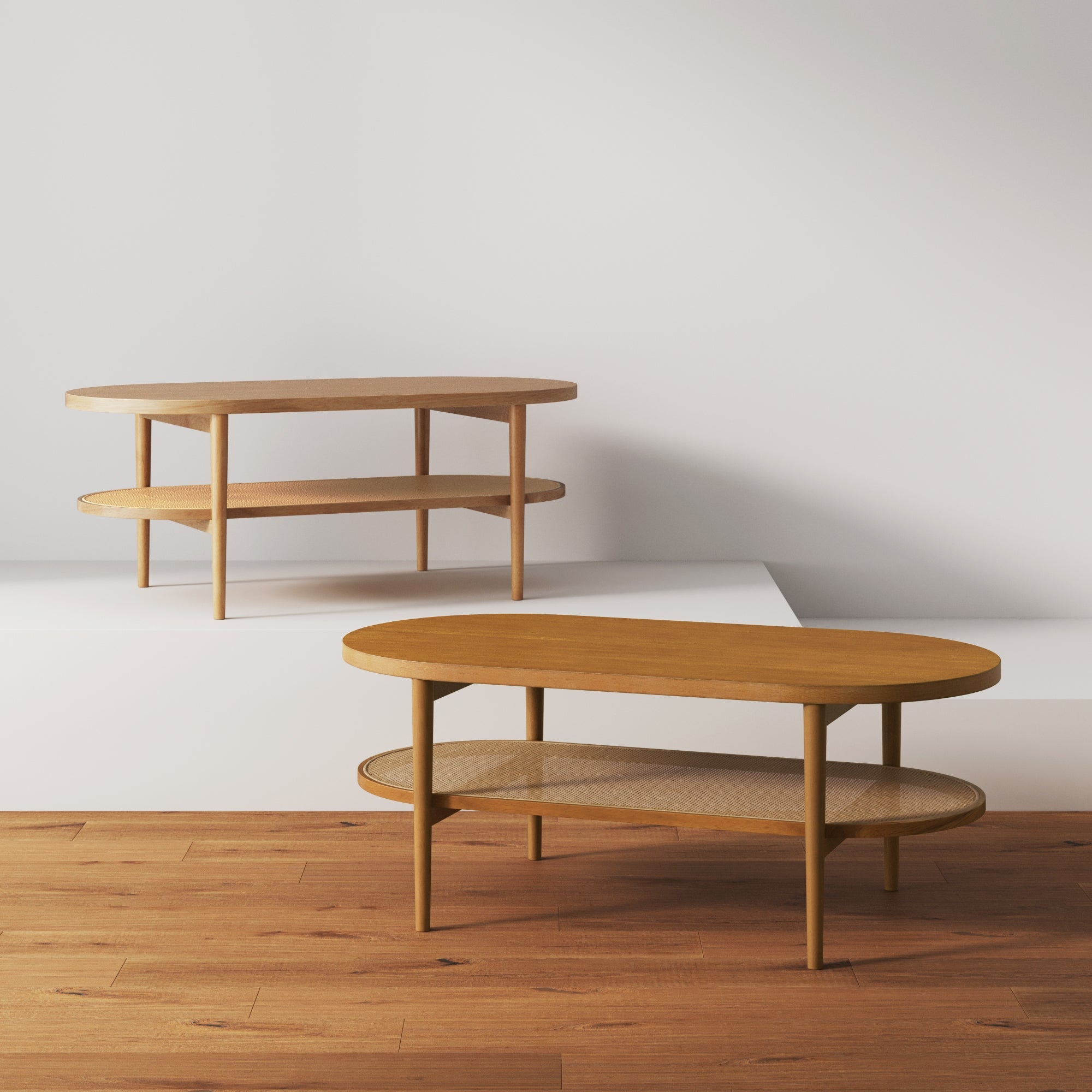 Two oval, wooden coffee tables with lower shelves are displayed in a minimalist room with light-colored walls and wooden flooring. One table is placed on a step in the background, and the other is in the foreground.