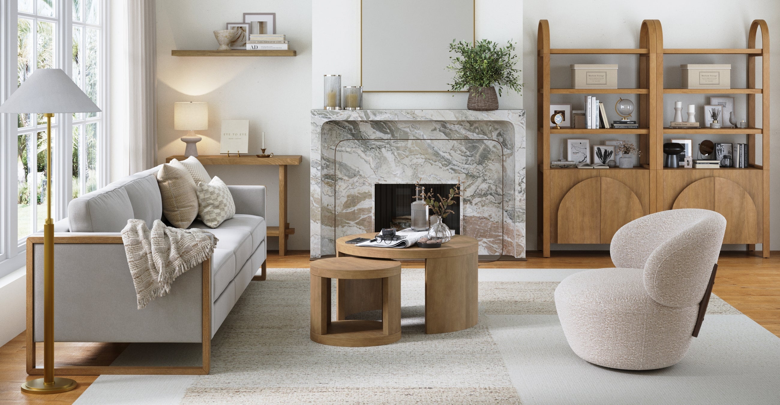 A modern living room with neutral tones features a light gray sofa, a round armchair, a marble fireplace, wooden coffee tables, open shelving, and large windows letting in natural light.
