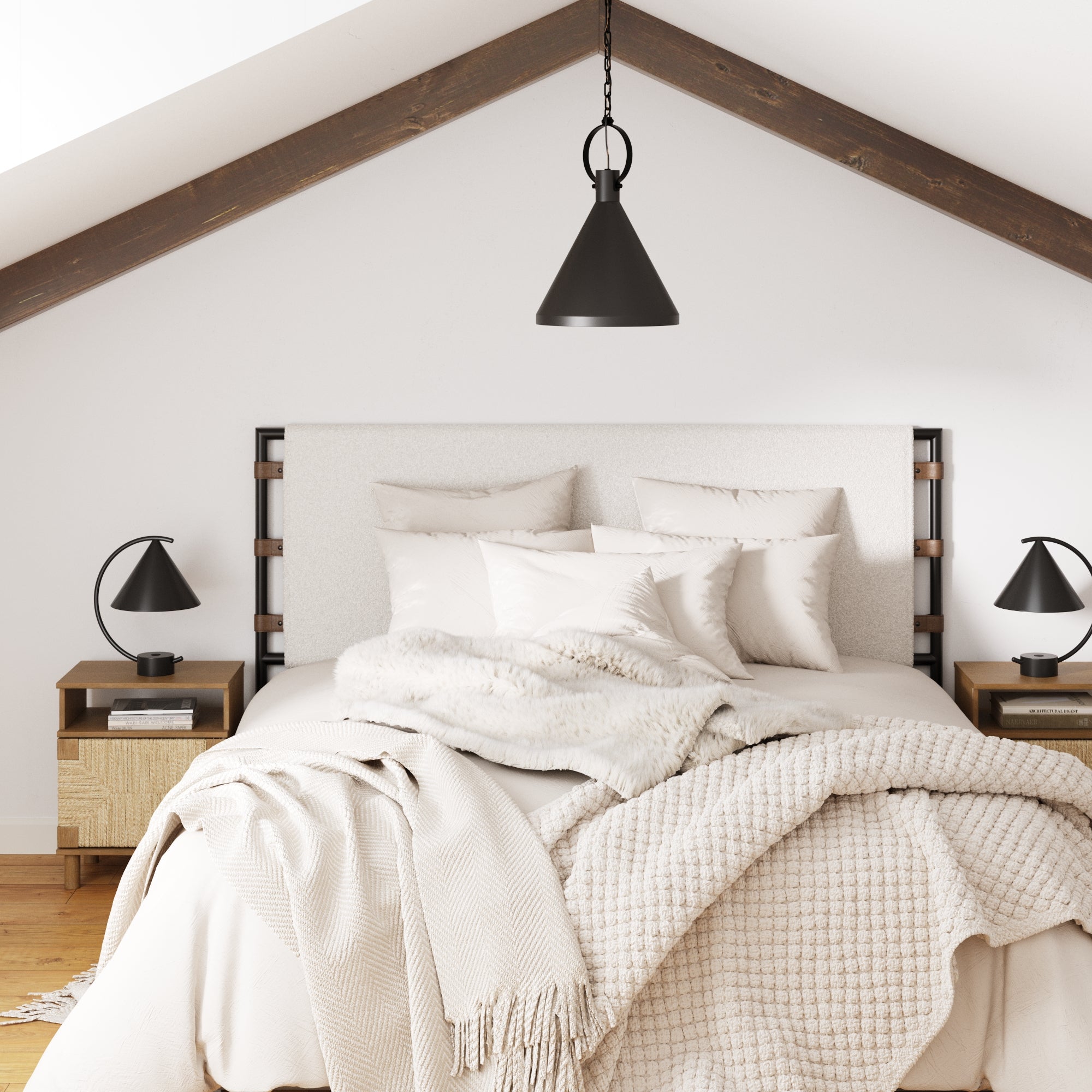 A cozy modern bedroom features a large bed with cream and beige blankets, accented by Nathan James Boho Seagrass Storage Nightstands (Set of 2) and a black lamp. Exposed dark beams and a black pendant light hang from the sloped ceiling.