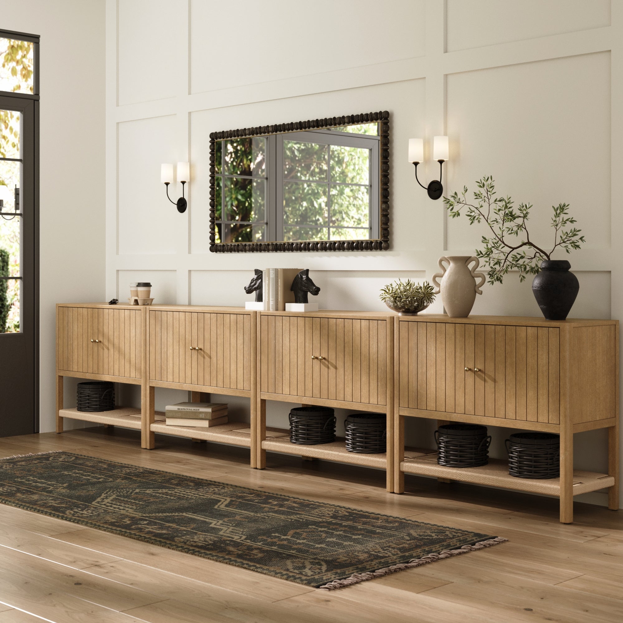 A modern entryway featuring four Nathan James Grooved Door Credenza TV Stand Storage Cabinets in light brown, decorative vases, wall sconces, a rectangular mirror, baskets on the lower shelves, and a patterned runner rug on light wood flooring.