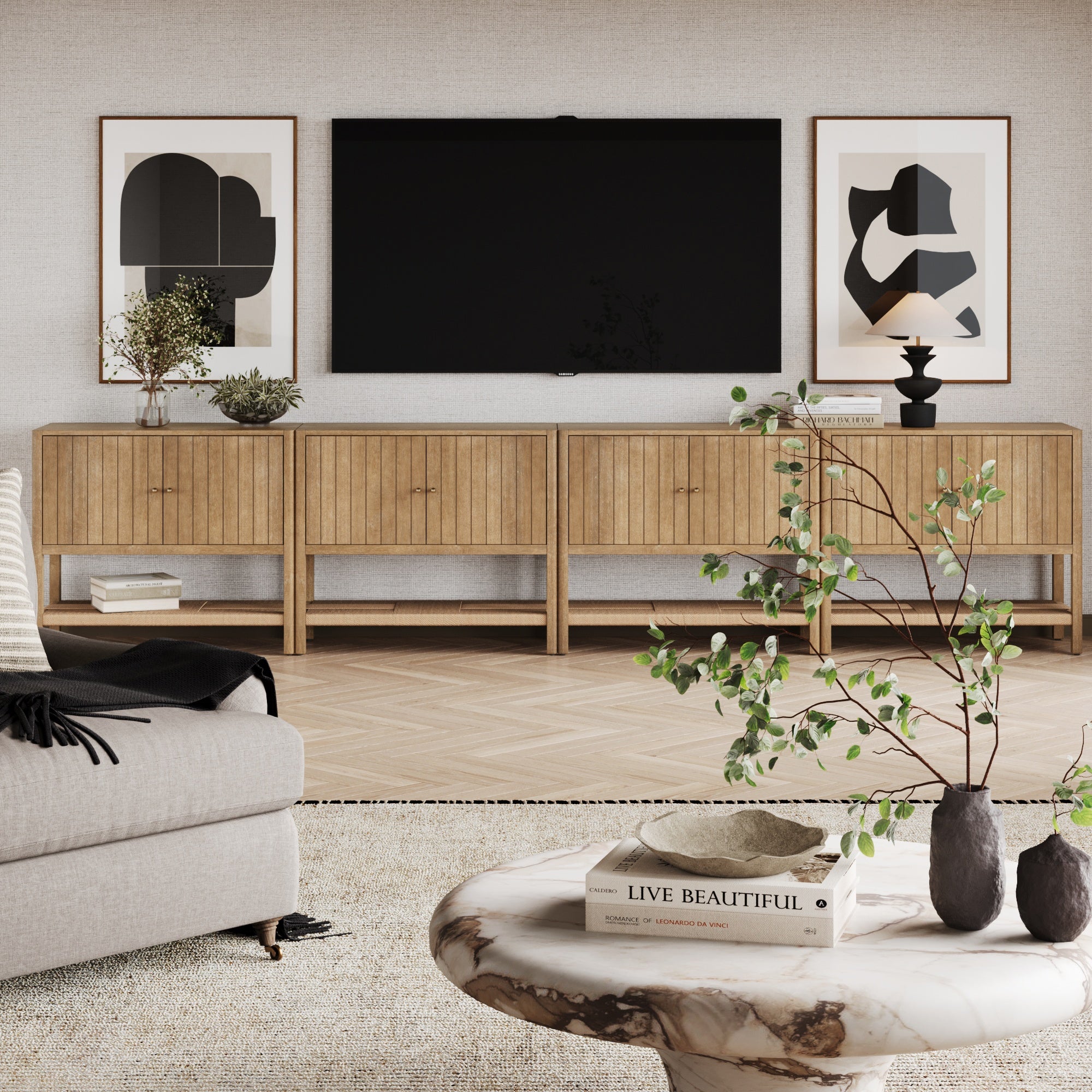 A modern living room features a marble coffee table, beige sofa, light wood media console, large TV, abstract art, decorative plants on a light rug and wood floor, plus the Nathan James Grooved Door Credenza TV Stand Storage Cabinet in Light Brown (Set of 4).