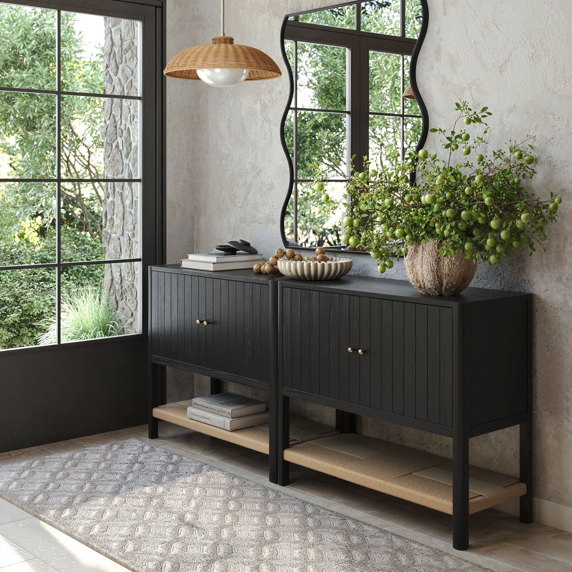 A modern entryway features two Nathan James Grooved Door TV Stand or Storage Cabinet units in black oak, a large mirror, pendant light, vase with green branches, sunlight streaming on a textured rug over the light wood floor.